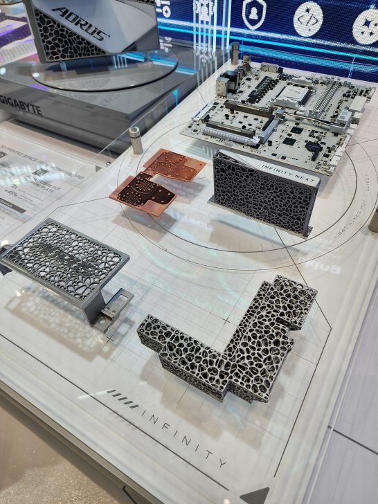 A Gigabyte Aorus display features a white motherboard alongside a piece labeled 'INFINITY NEXT' with a distinctive lattice design.