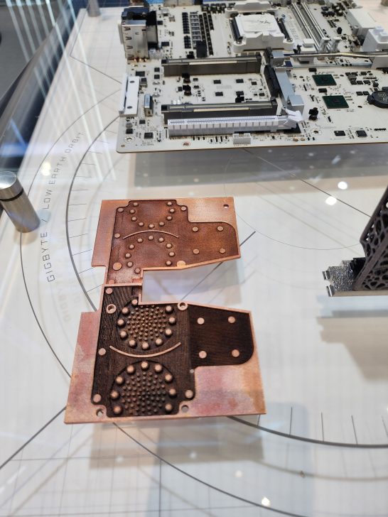 A Gigabyte motherboard is displayed alongside a copper heat sink under a glass case labeled 'GIGABYTE LOW EARTH ORBIT.'