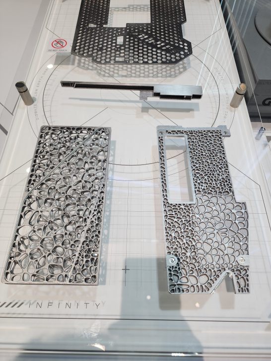 Two intricately patterned metal components labeled 'INFINITY' on a display with a 'DO NOT TOUCH' sign visible.