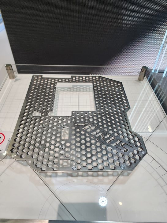 A metal backplate with a hexagonal pattern and the 'AORUS' logo is displayed on a glass surface.