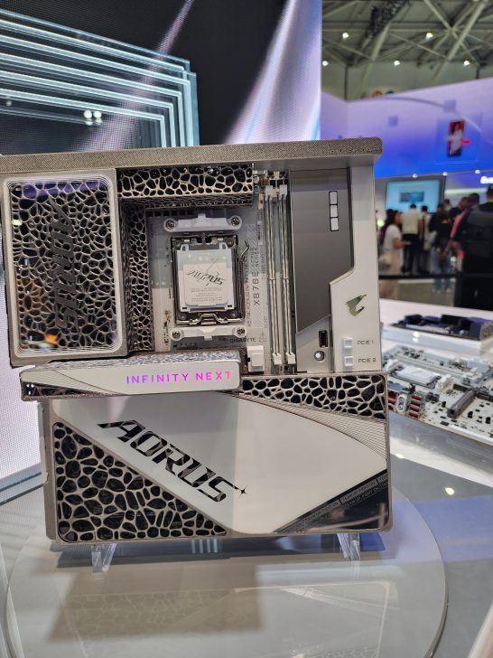 A showcase of a Gigabyte AORUS motherboard featuring 'INFINITY NEXT' lighting on display at an exhibition.