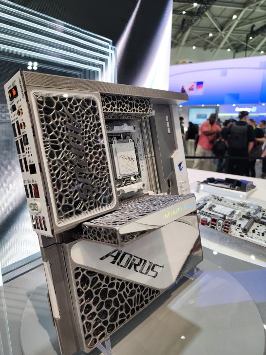 A futuristic desktop case by AORUS featuring intricate lattice designs and labeled 'INFINITY NEXT' is displayed at a technology exhibition.