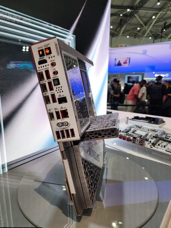 An AORUS gaming desktop with a visible rear I/O panel and multiple USB ports is displayed prominently at a tech exhibition.