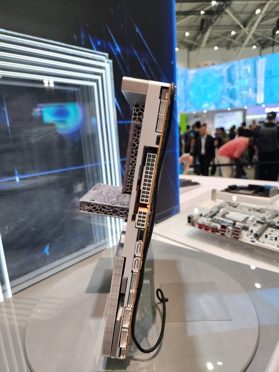 A side view of an unbranded graphics card with multiple power connectors and a unique cooling design displayed at a tech exhibition.