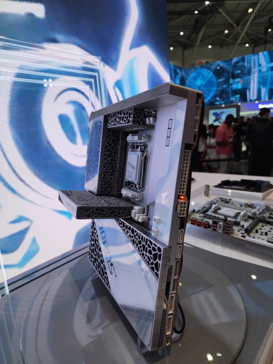 A side view of the AORUS water-cooled NVMe SSD showcased on a display, featuring a futuristic hexagonal vent design and visible branding.