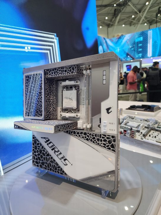 An AORUS display showcasing a futuristic open-frame motherboard concept with the text 'INFINITY NEXT' visible on the side, during a technology exhibition.