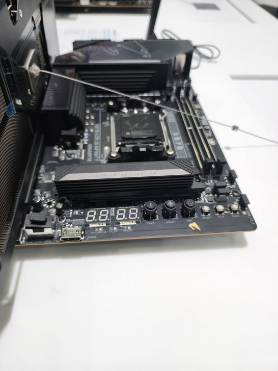 A Gigabyte Aorus Z790 motherboard with visible 'Aorus Design Lab' branding and a digital display showing '0.0.0.0'.