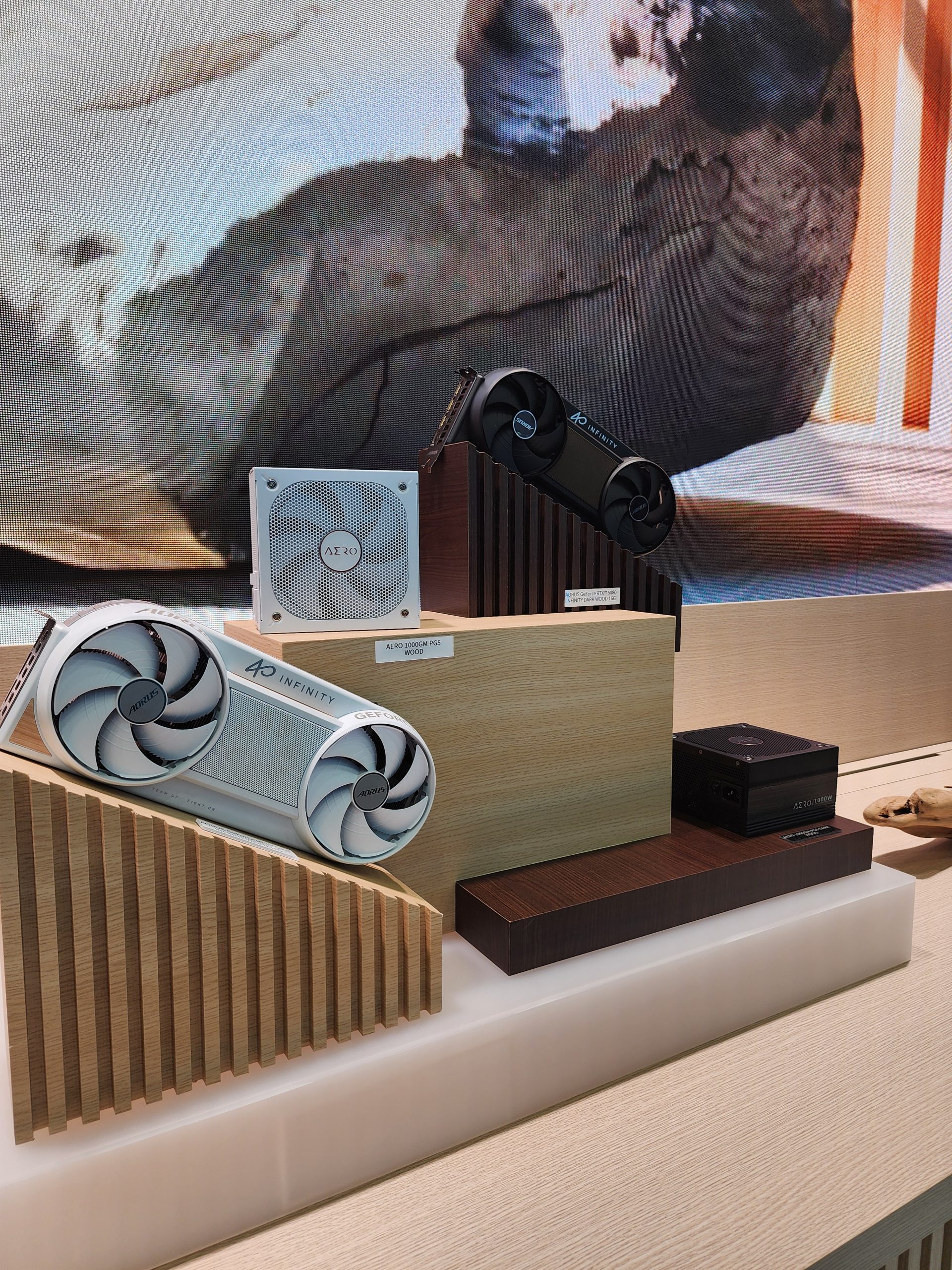 Gigabyte AORUS GeForce RTX 40 series GPUs and an AERO power supply are displayed on a wooden stand with the labels 'AERO Design PC DIY' and 'AORUS 700 GOLD PSU MF3'.