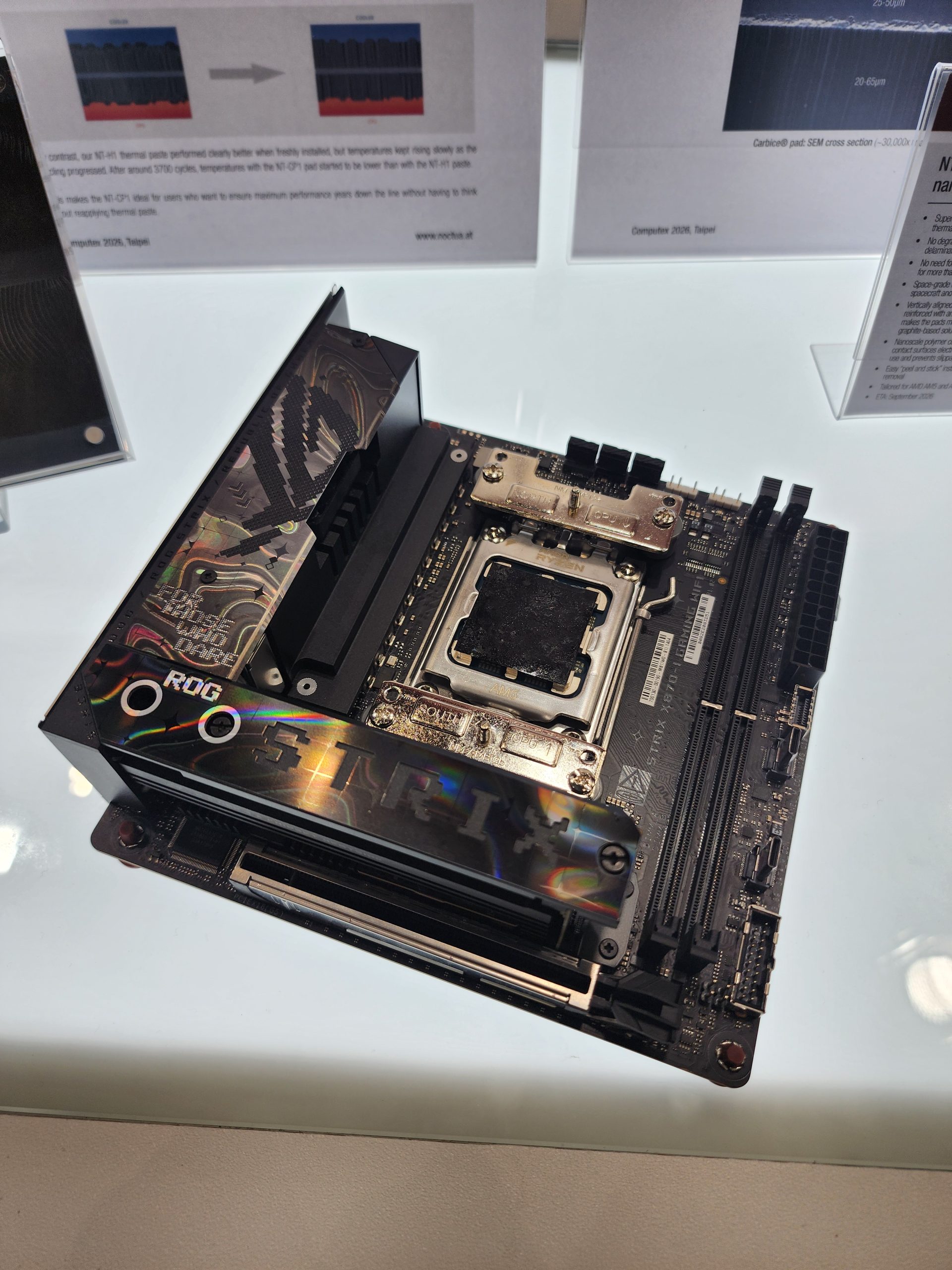 An ASUS ROG Strix motherboard is displayed on a table, featuring an exposed CPU socket and visible branding.