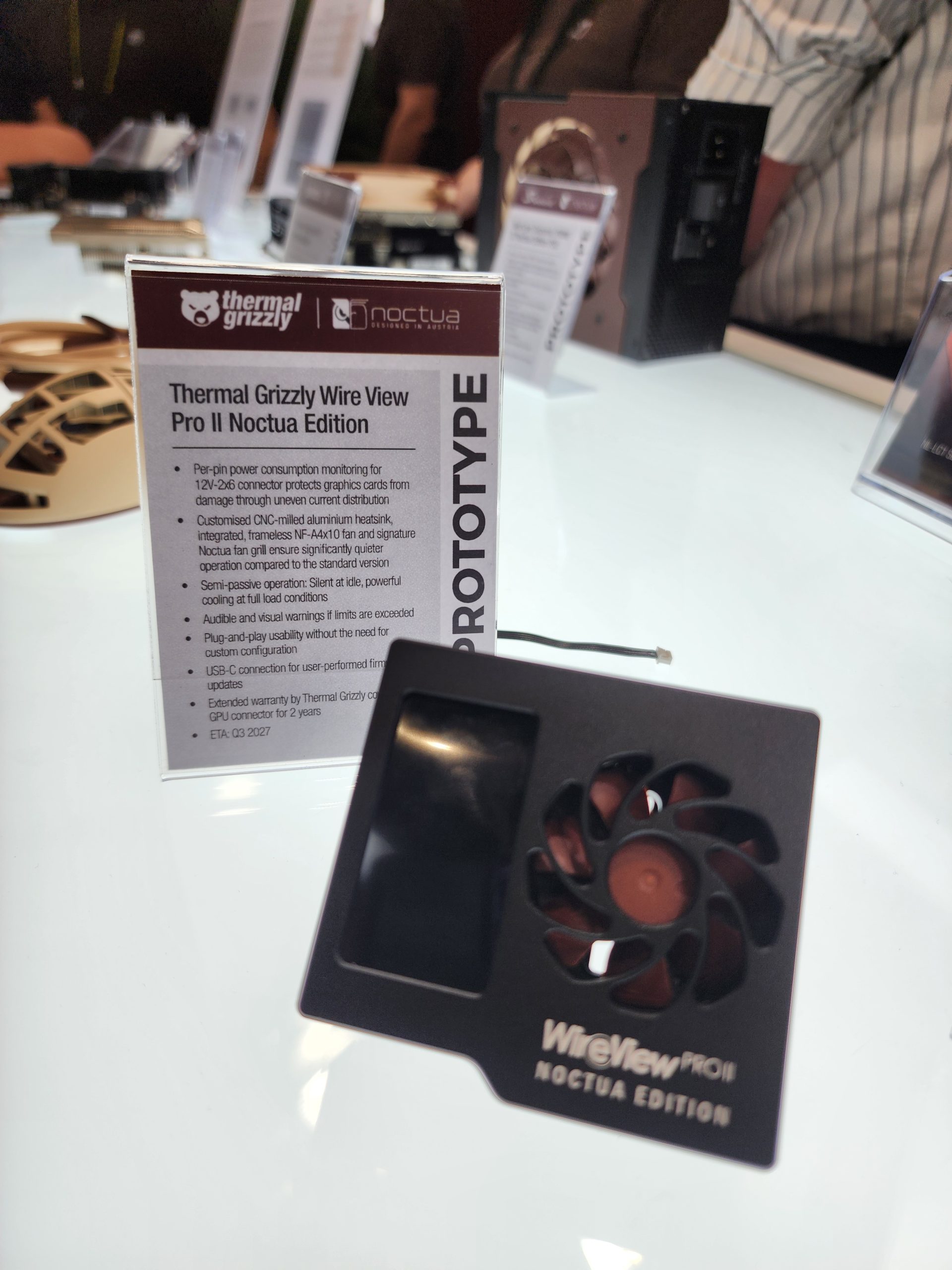 A Thermal Grizzly Wire View Pro II Noctua Edition prototype is displayed on a table, with informational text in the background detailing its features and specifications.