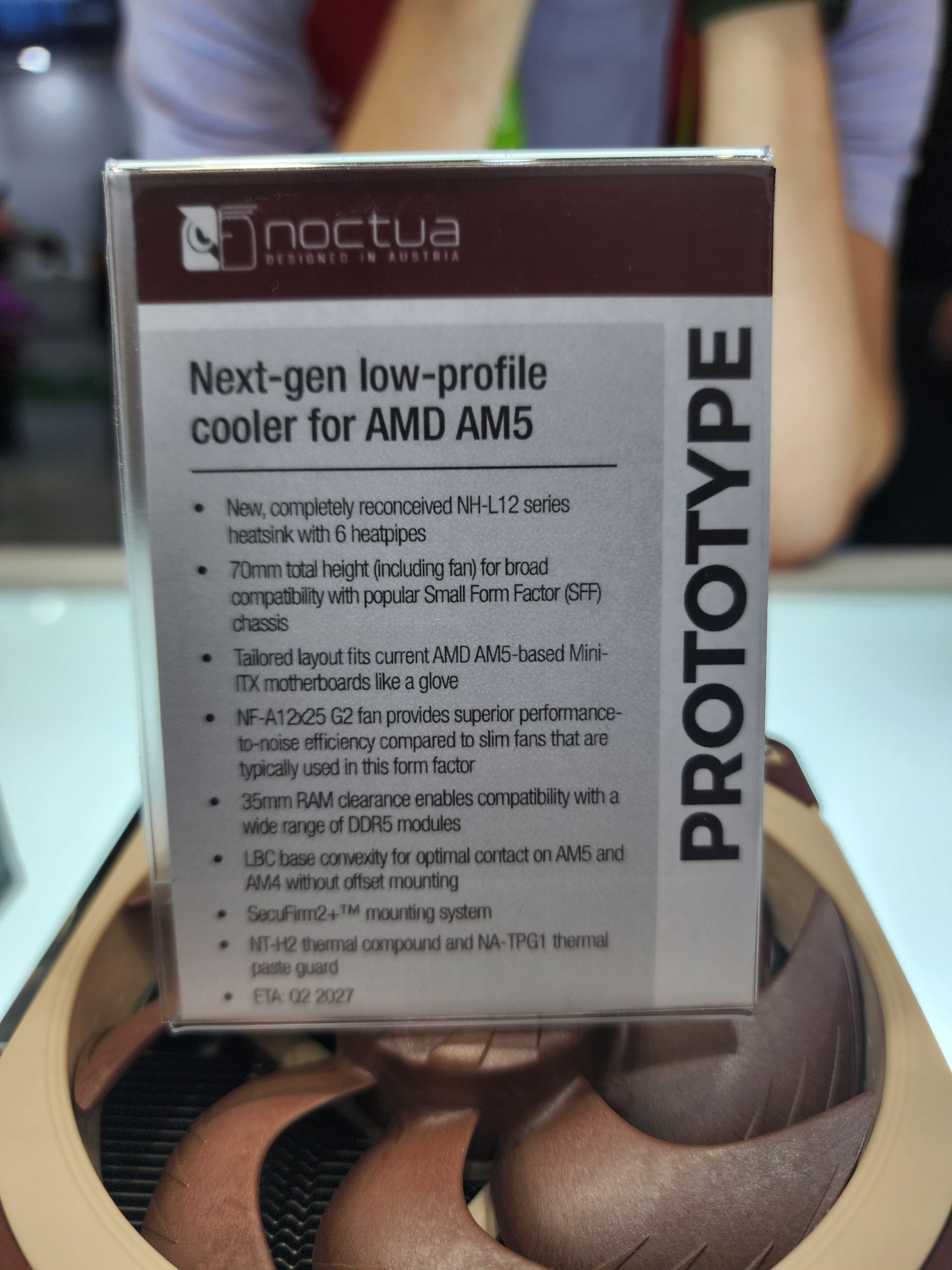 A Noctua display shows a sign for a Next-gen low-profile cooler for AMD AM5 with details about its NH-L12 series heatsink, NF-A12x25 G2 fan, and features like 70mm total height and 35mm RAM clearance.