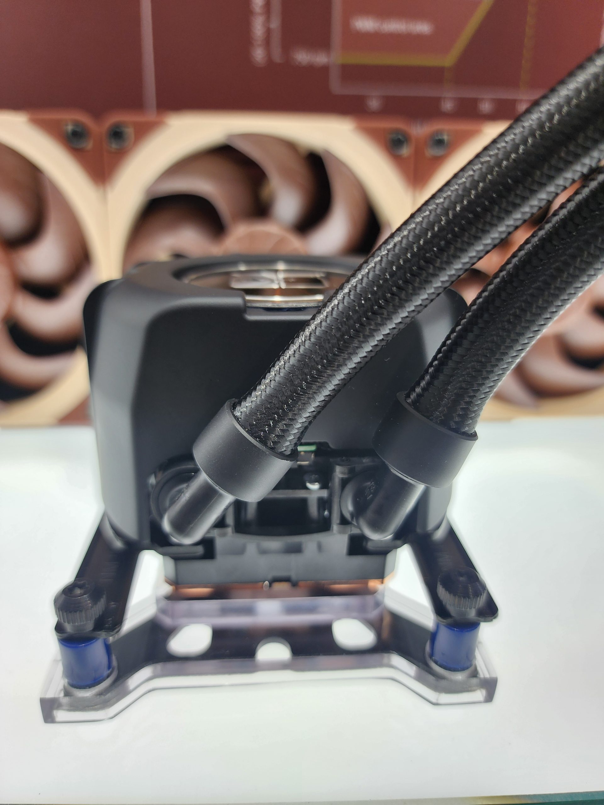A Noctua cooling system with braided tubes is mounted on a stand, with large brown fans visible in the background.