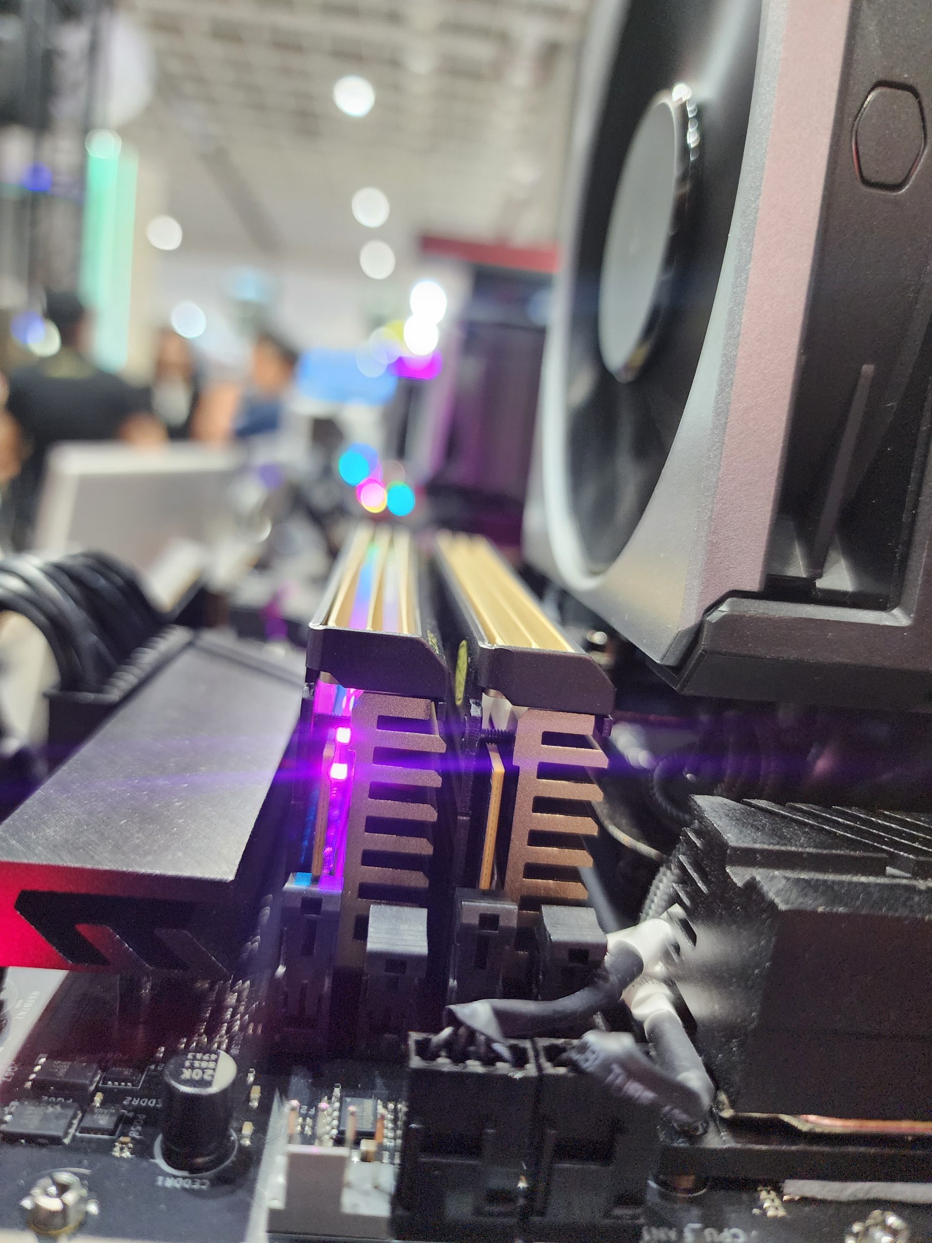 Close-up of RGB-lit RAM modules installed on a motherboard beside a large cooling fan.