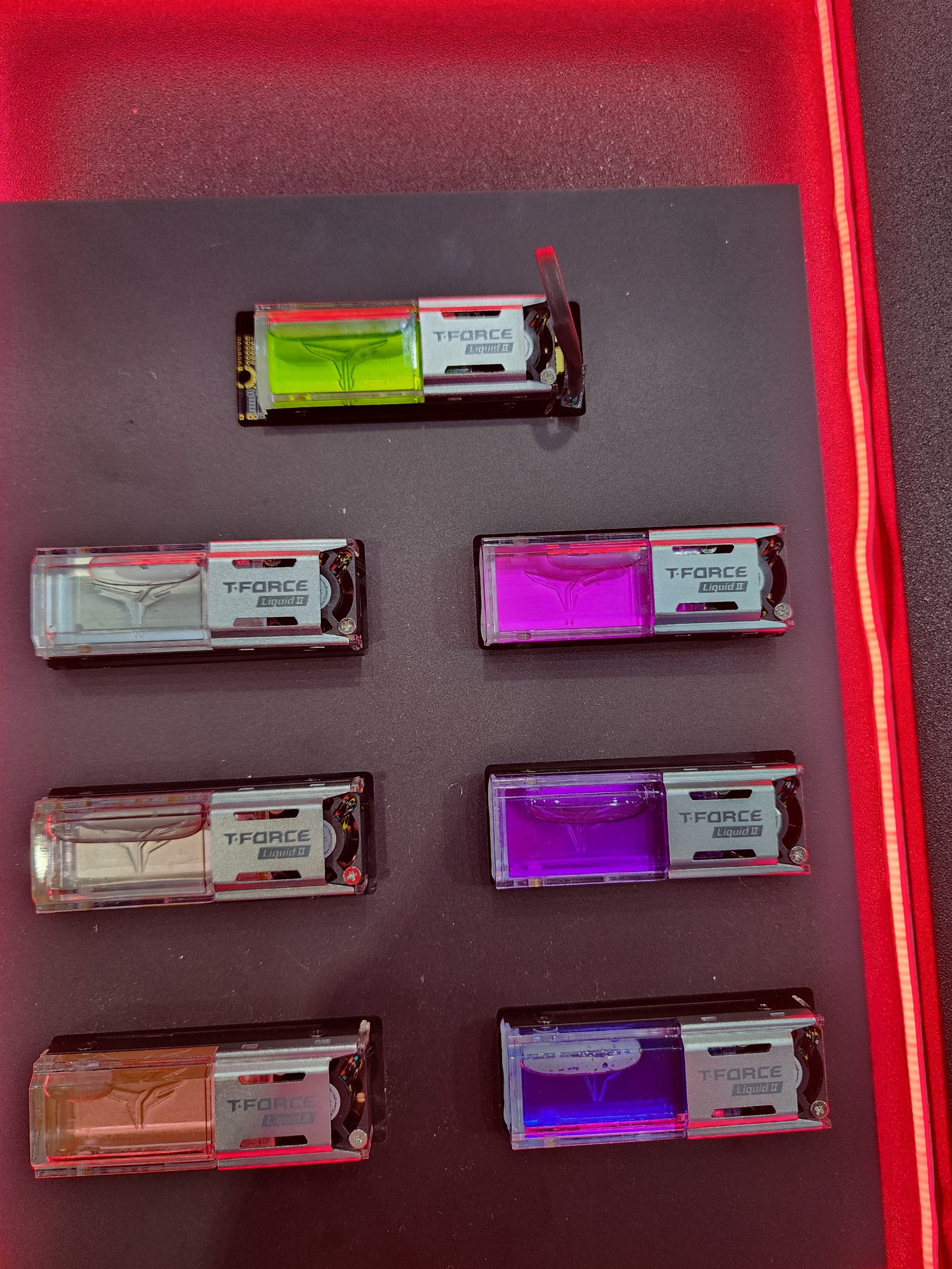 Six T-Force Liquid II memory modules with visible liquid cooling chambers in various colors on display.