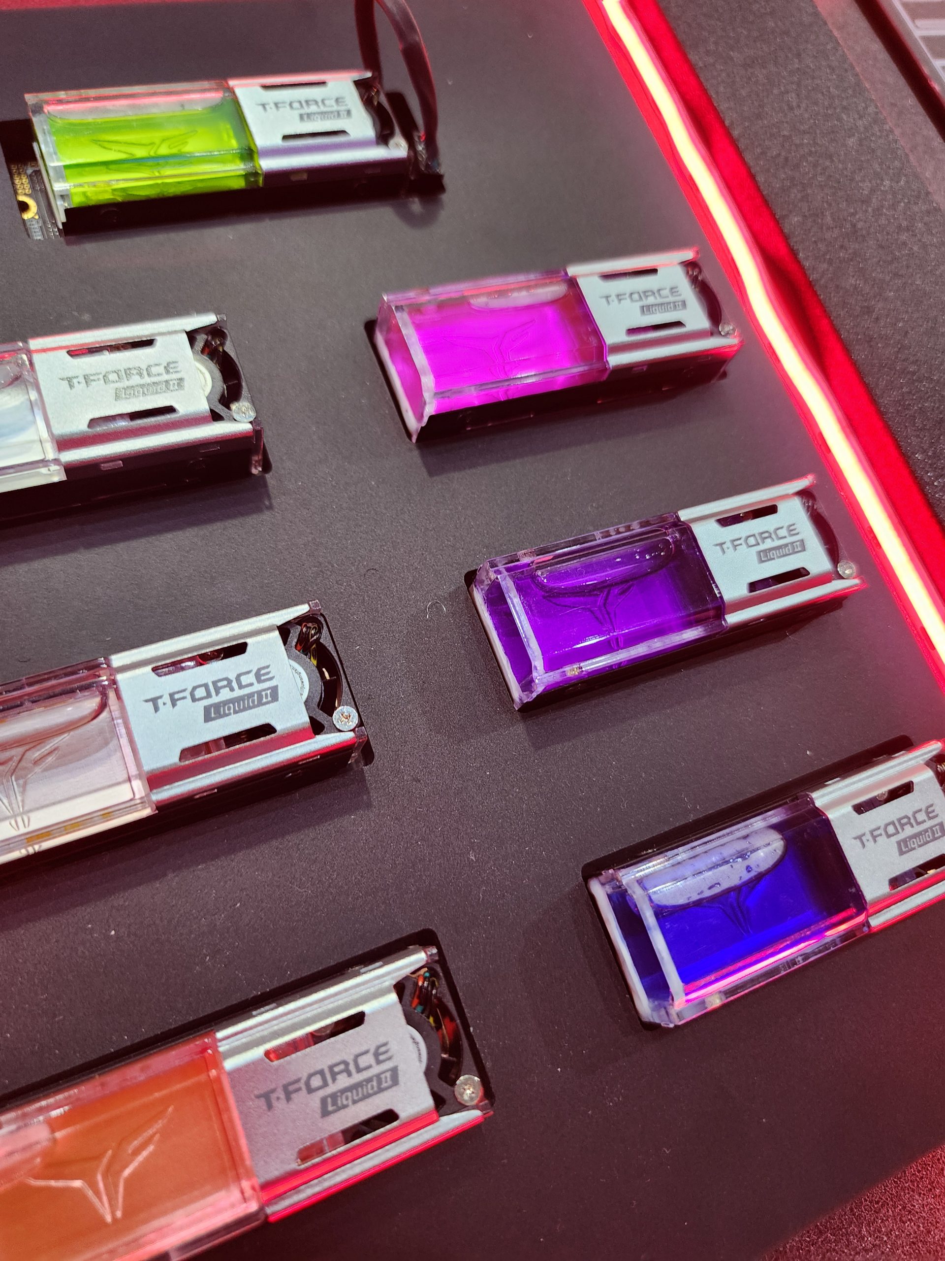 Six TeamGroup T-FORCE Liquid II SSDs in various colors are displayed in a showcase.