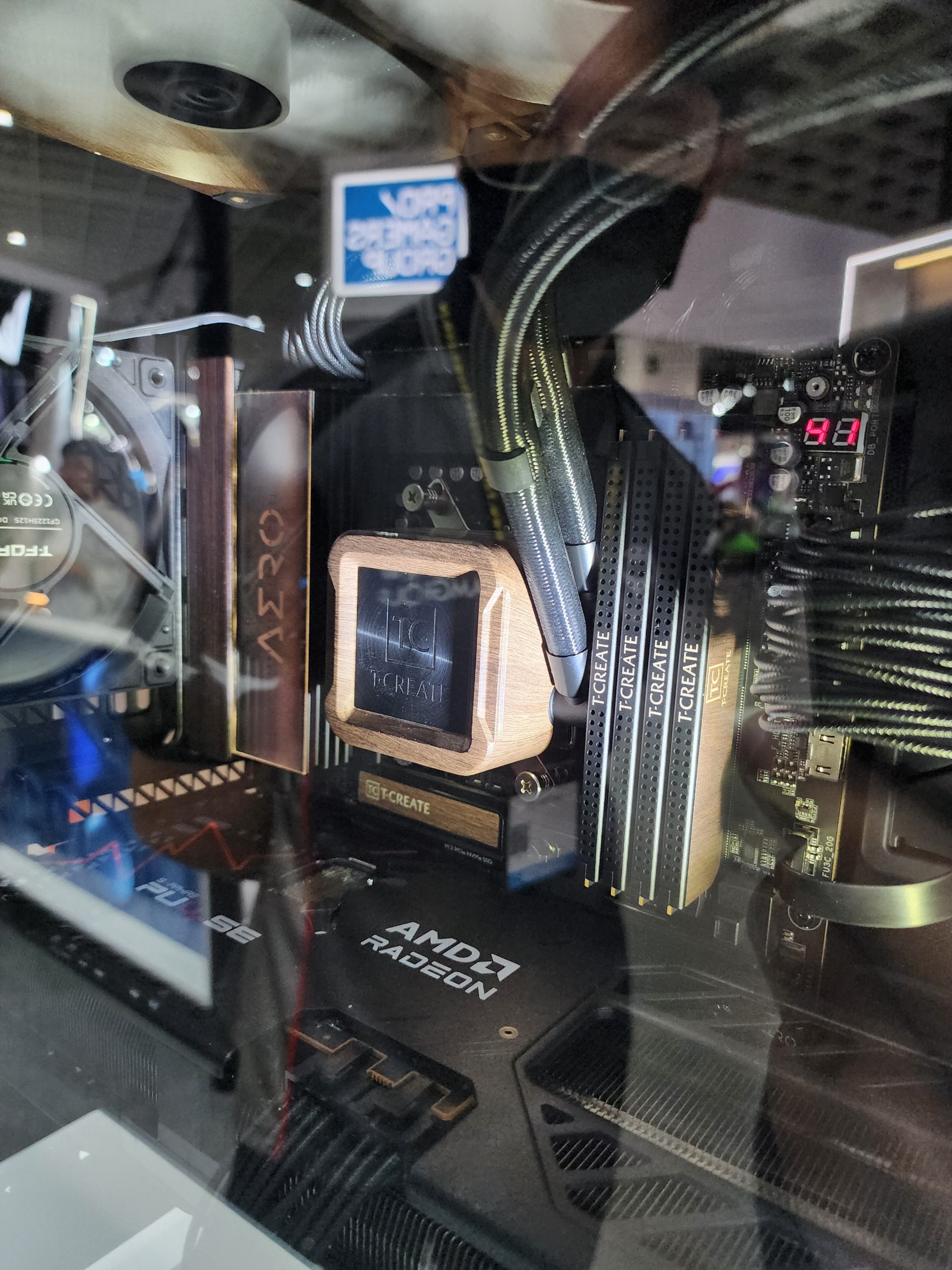 A close-up view of a PC build features an AMD Radeon graphics card, T-Create branded components, and an on-board display showing '91'.