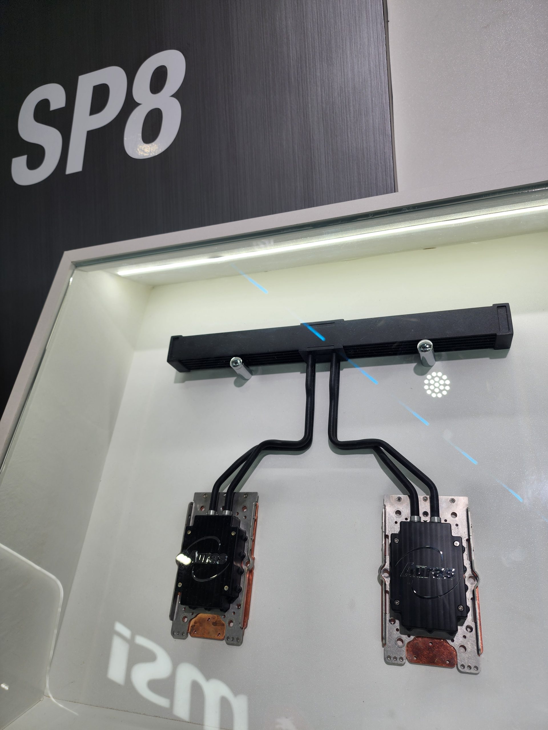 A showcase display features two metal cooling devices labeled SP8, with the brand Aurec visible on each, inside a cabinet with the MSI logo reflected on the glass.