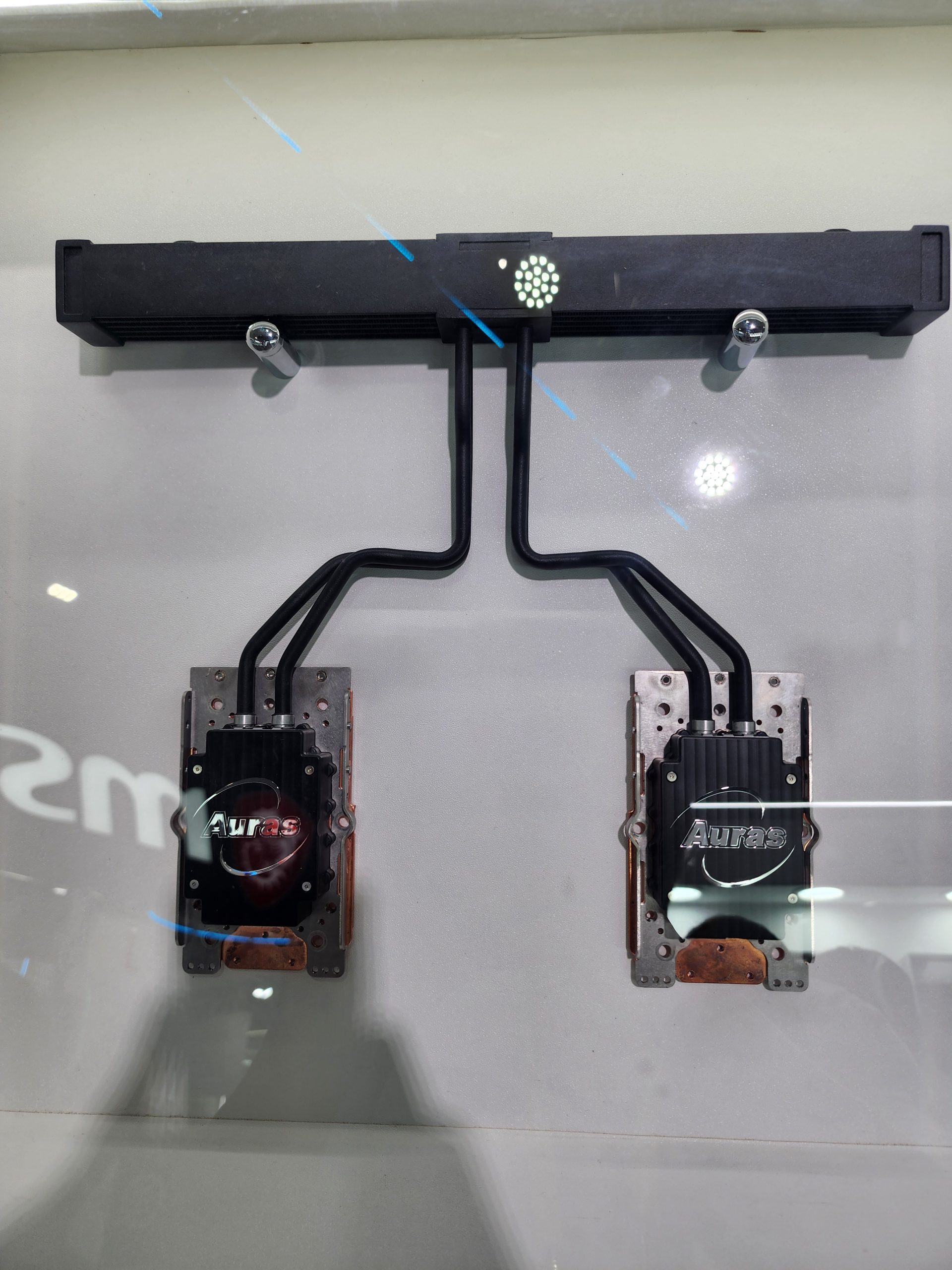 A display of dual Auras cooling heat sinks connected to a black radiator bar mounted on a vertical surface.