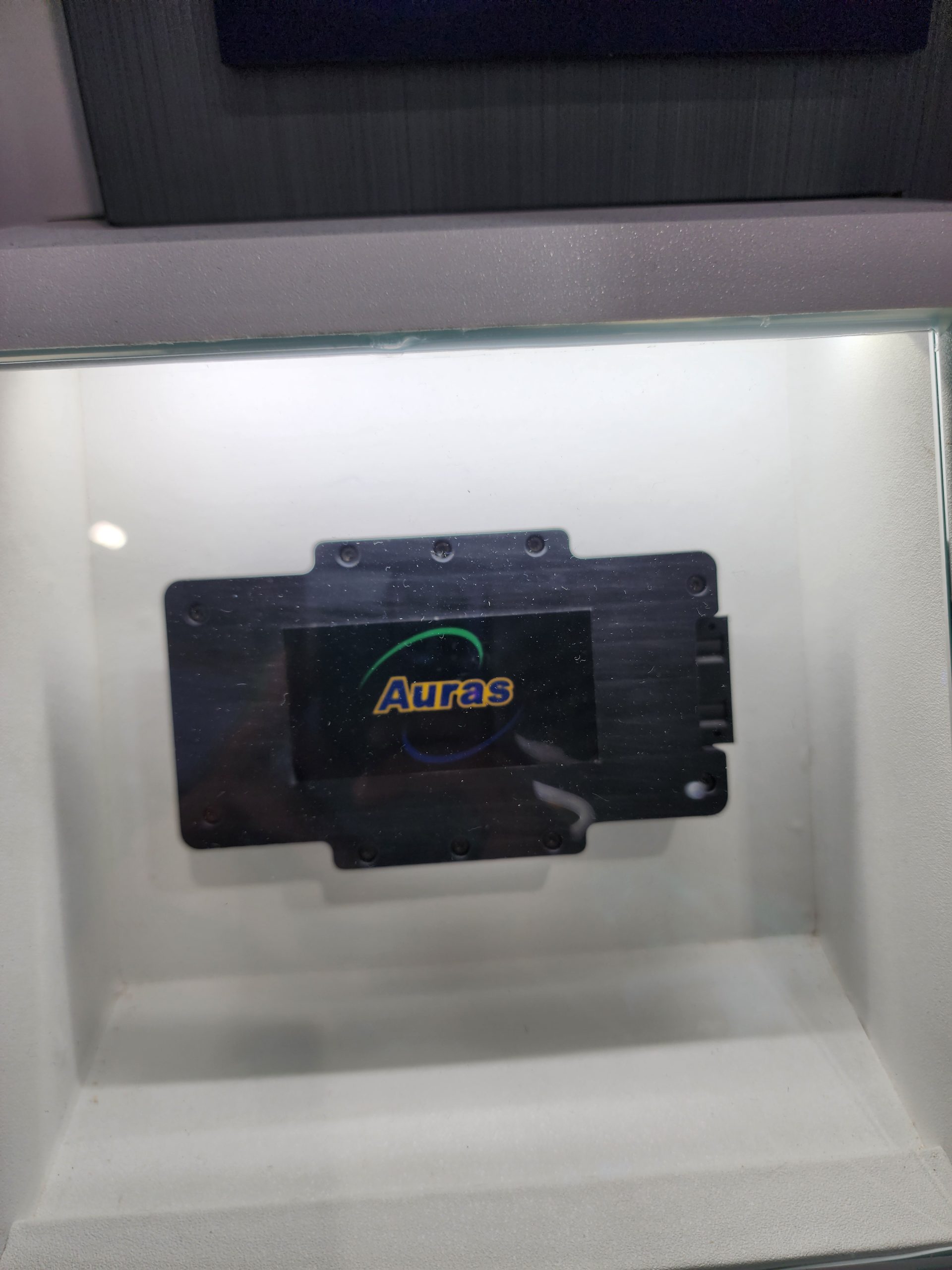 A black cooling component with the logo 'Auras' displayed inside a glass showcase.