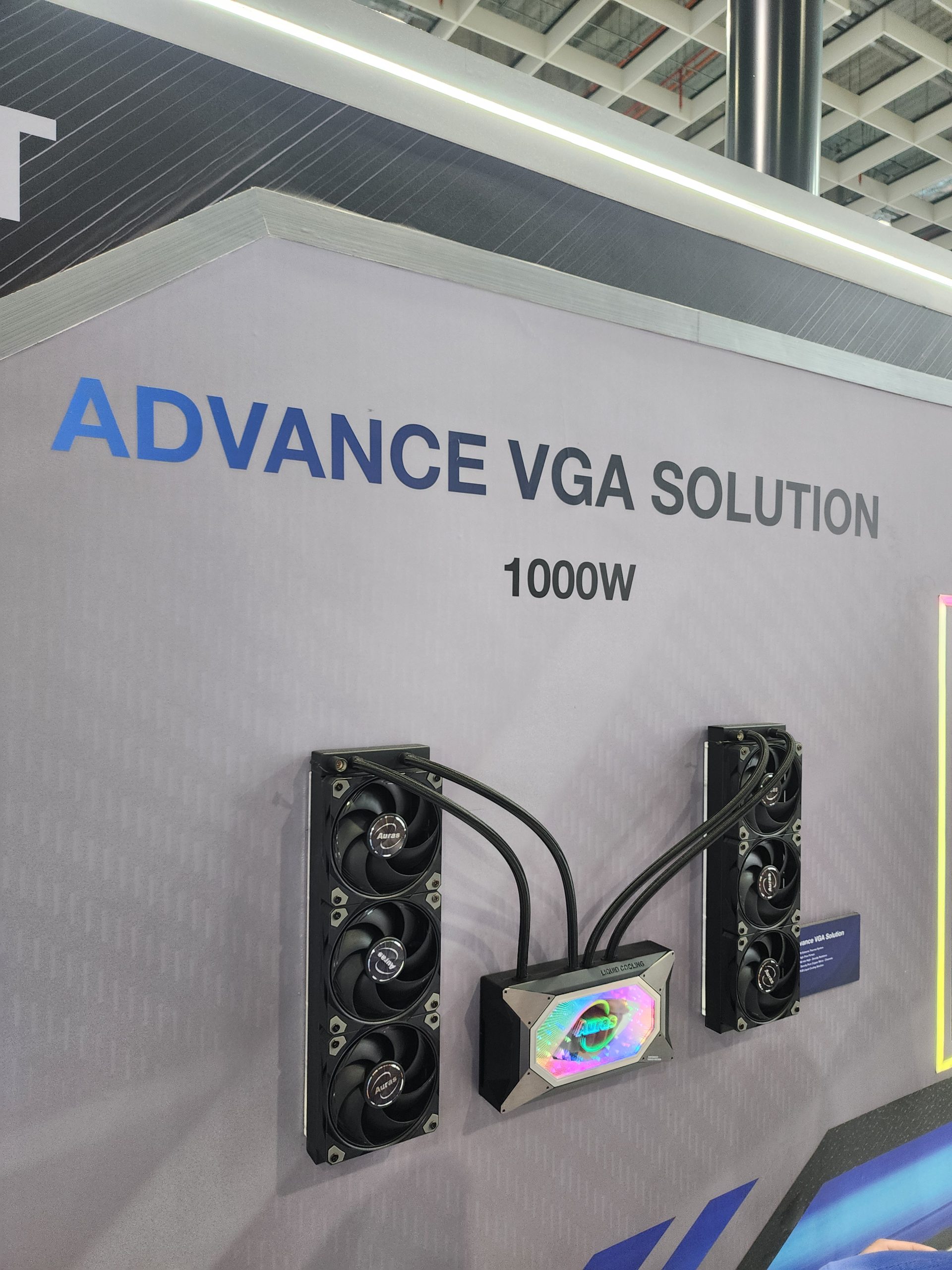 A wall display showing an 'ADVANCE VGA SOLUTION 1000W' with two Aorus-branded cooling units connected to a central liquid cooler block.