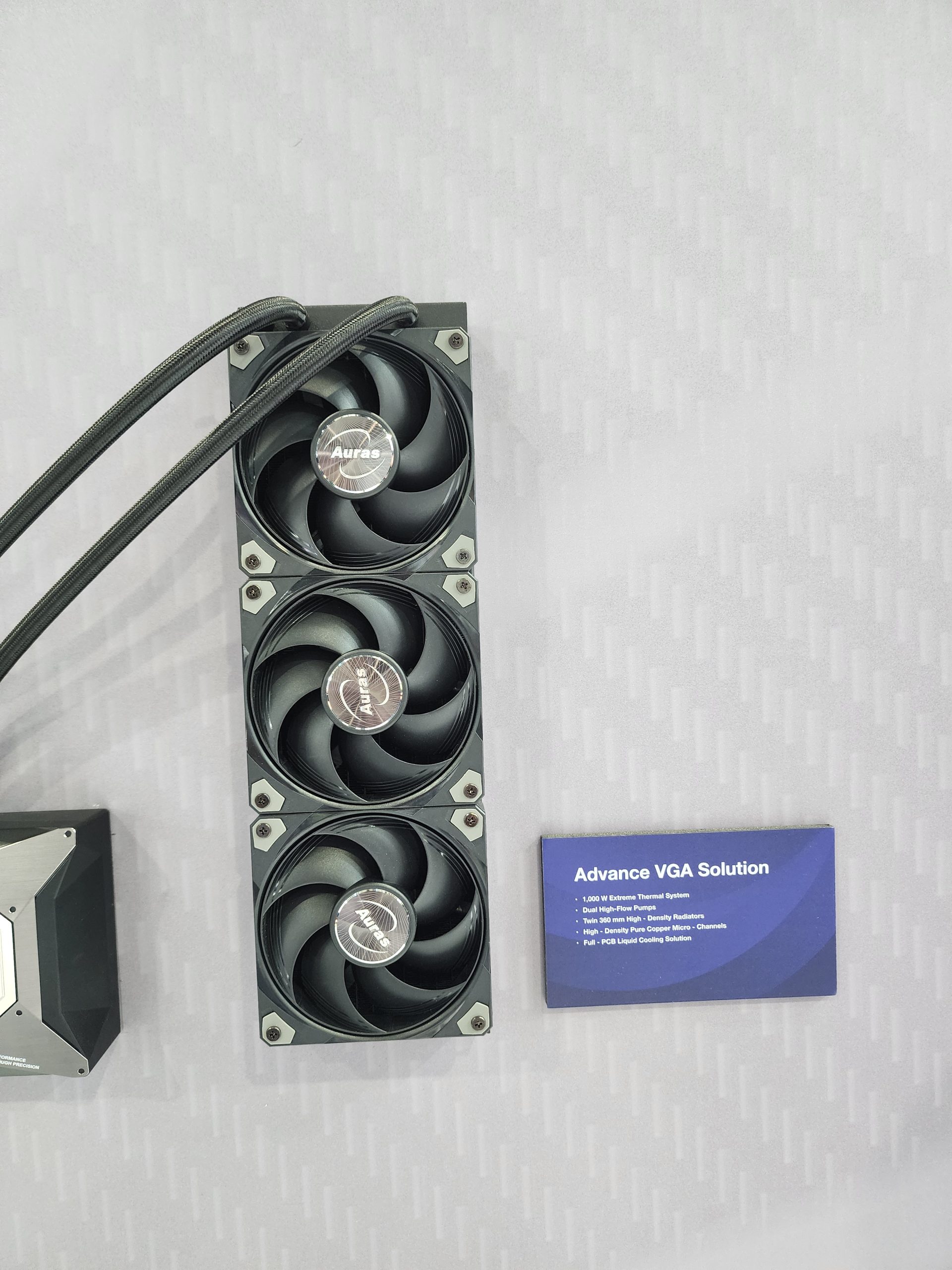 A vertical array of three black fans with Auras branding next to a sign titled 'Advance VGA Solution' listing features like a 1,000W extreme thermal system and dual Hi-Flow pump.