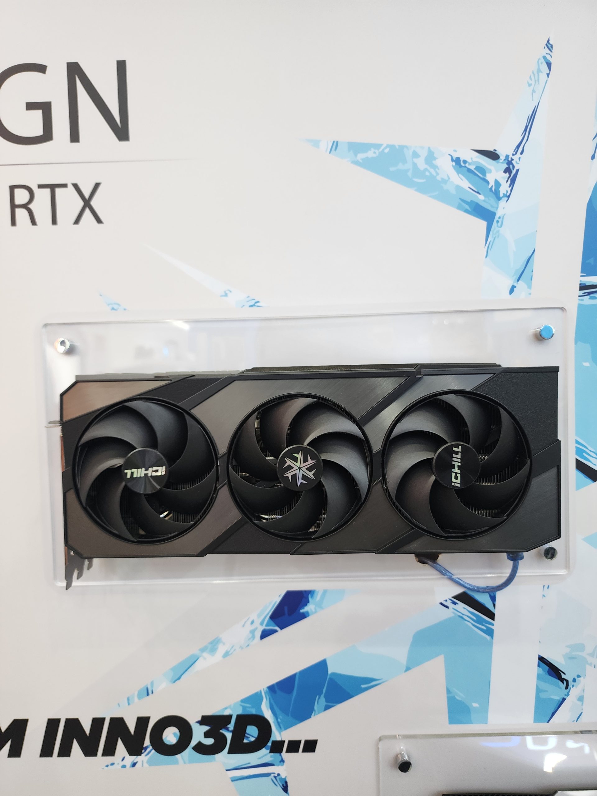 A black Inno3D GeForce RTX graphics card with 'iCHILL' branding is displayed against a backdrop with blue geometric patterns.