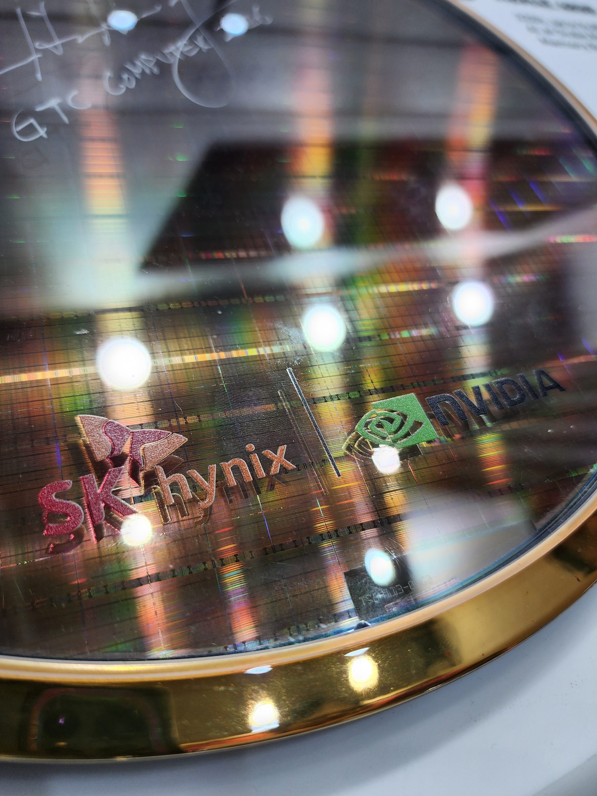 A close-up of a semiconductor wafer displaying the logos of SK hynix and NVIDIA, with some light reflections.