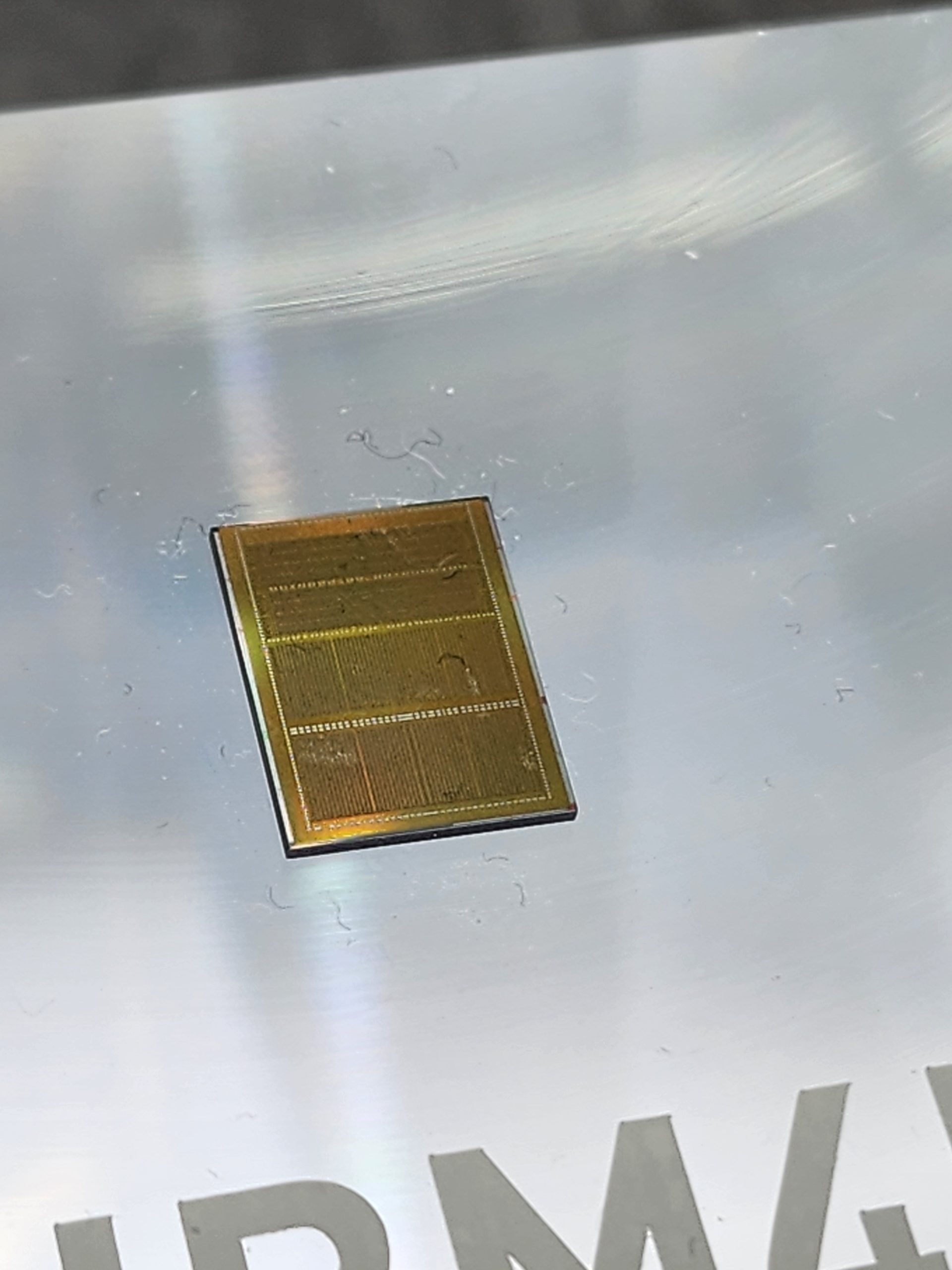 A close-up view of a silicon wafer prototype displayed on a reflective surface with partially visible text 'IBM'.