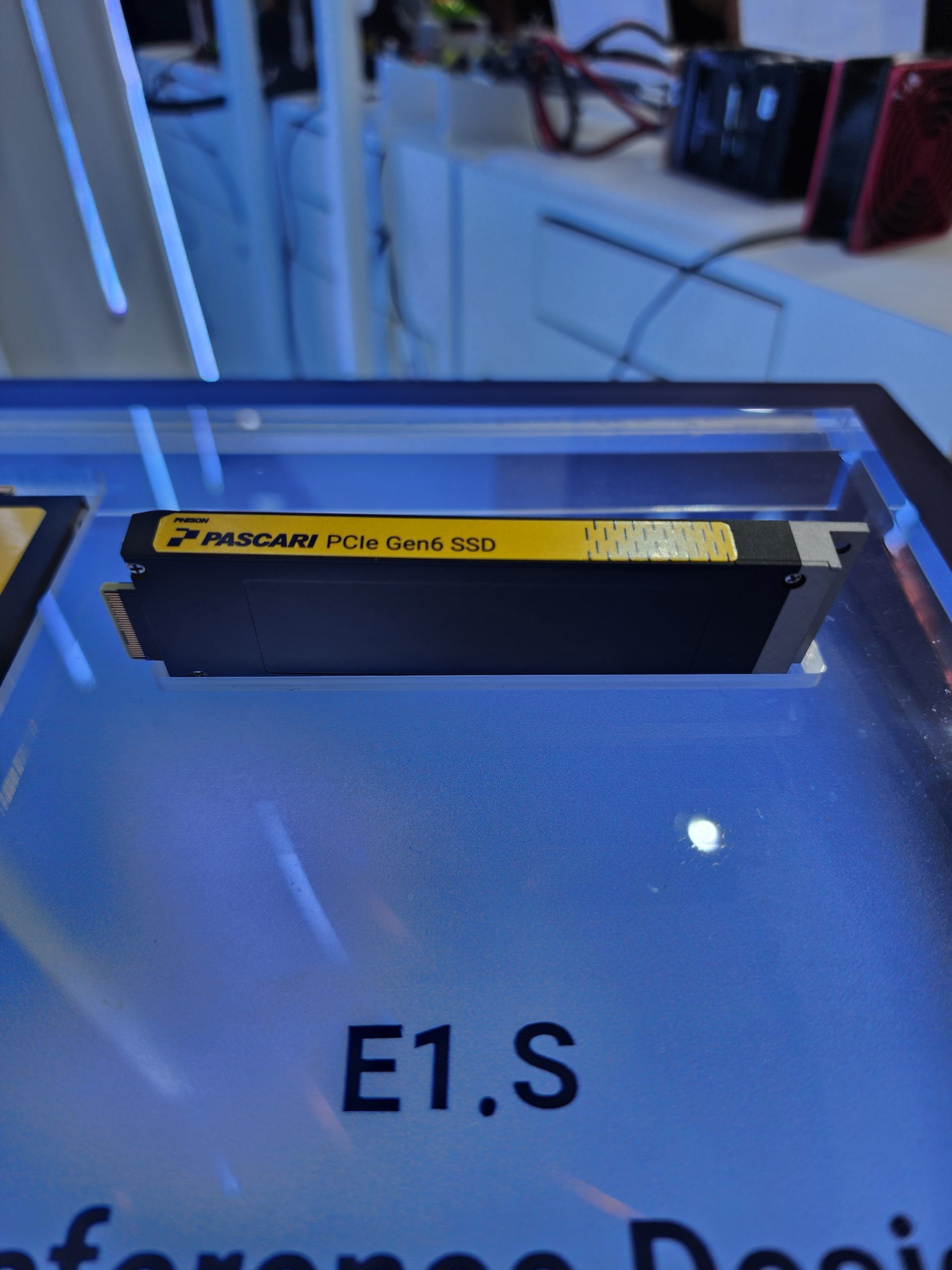 A PASCARI PCIe Gen6 SSD labeled 'E1.S' is displayed in a showcase with other tech components in the background.