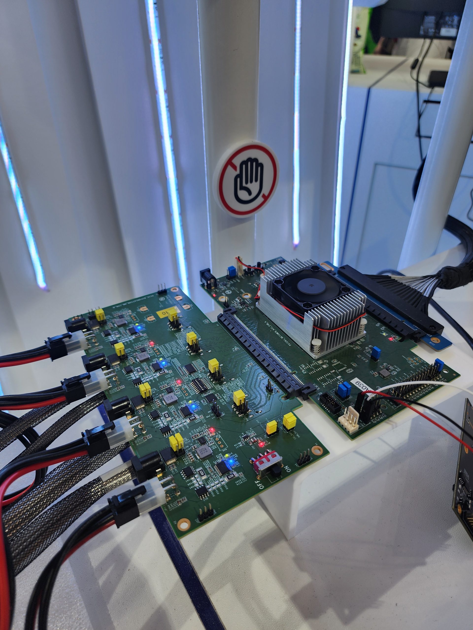 A circuit board with various components and connectors is displayed, with a heat sink attached, next to a 'no touch' sign.