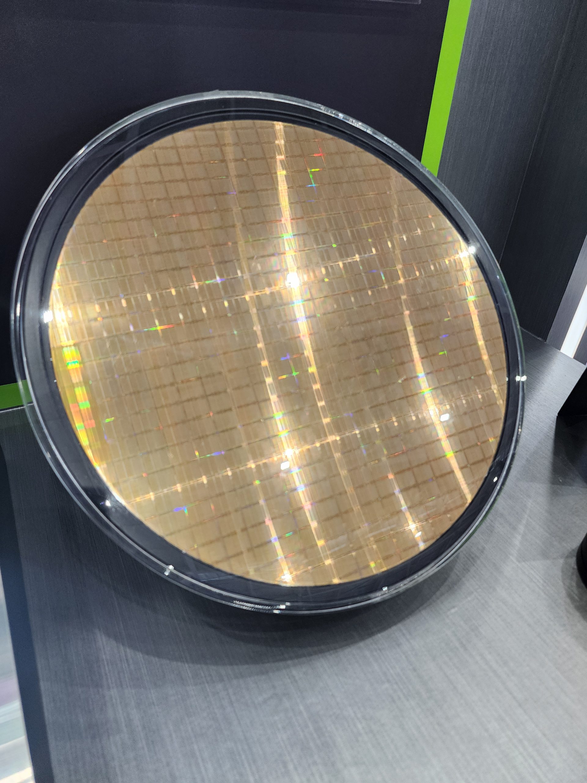 A silicon wafer reflecting light, displayed vertically on a gray surface.