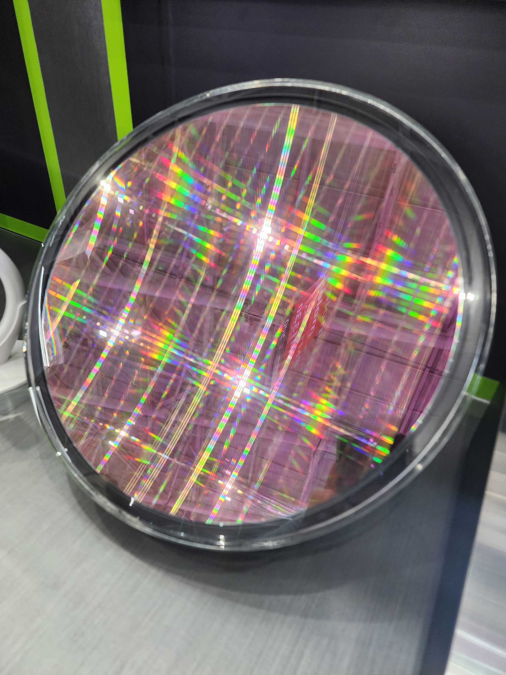 A circular silicon wafer with a rainbow pattern reflects light on a display table.