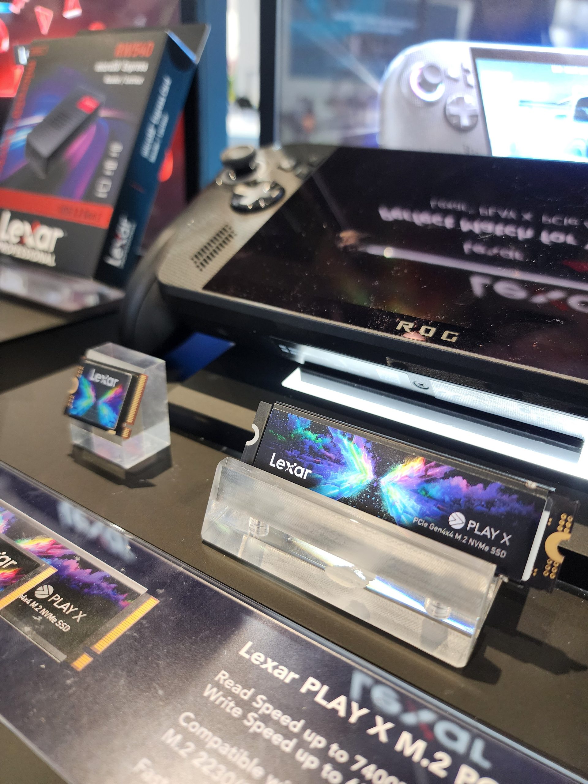 A Lexar PLAY X PCIe Gen4x4 M.2 NVMe SSD and packaging are displayed next to an ROG gaming device.