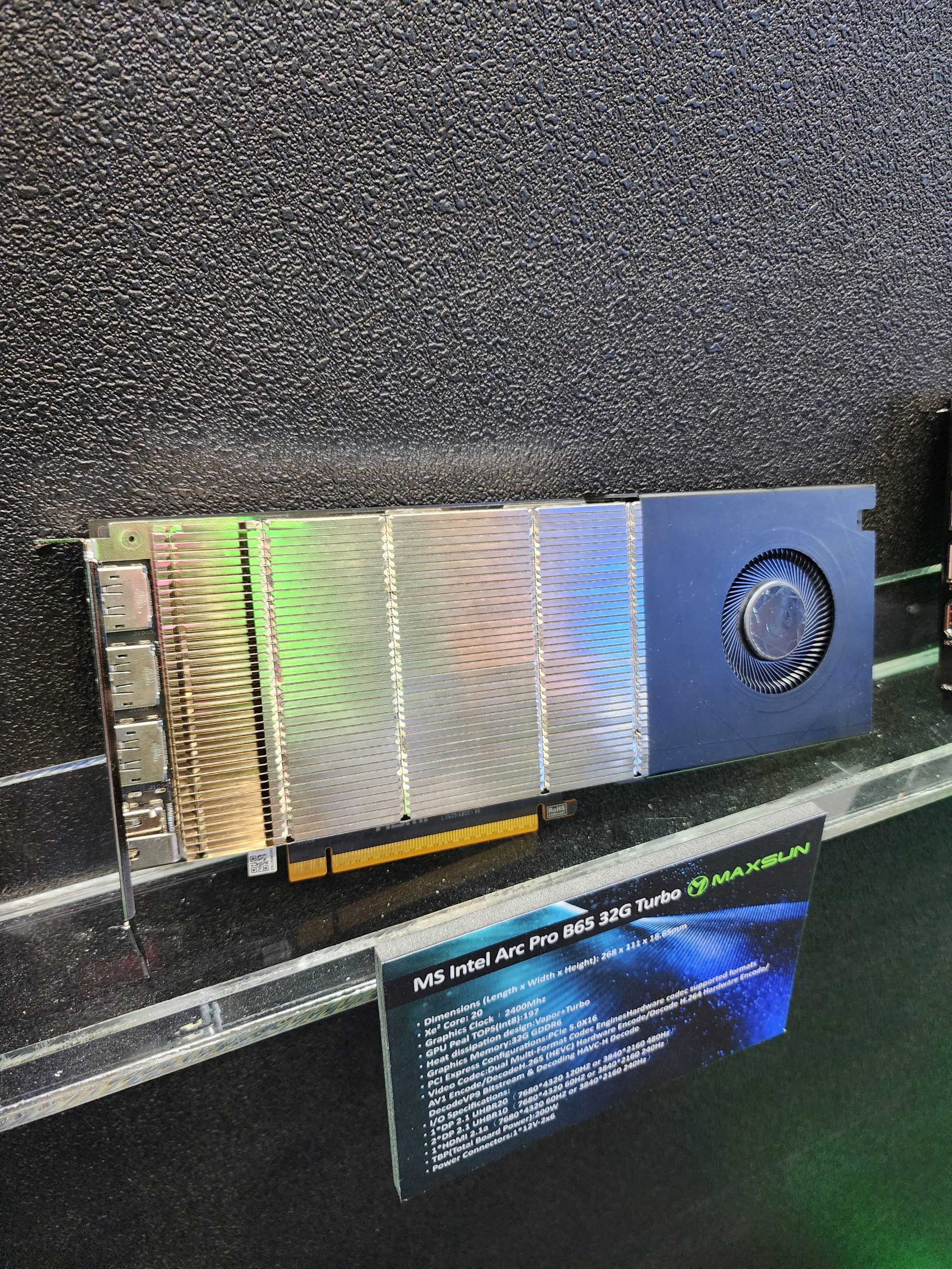 The image shows an MS Intel Arc Pro B65 32G Turbo graphics card with a prominent cooling fan and a plaque detailing its specifications, displayed by Maxsun.