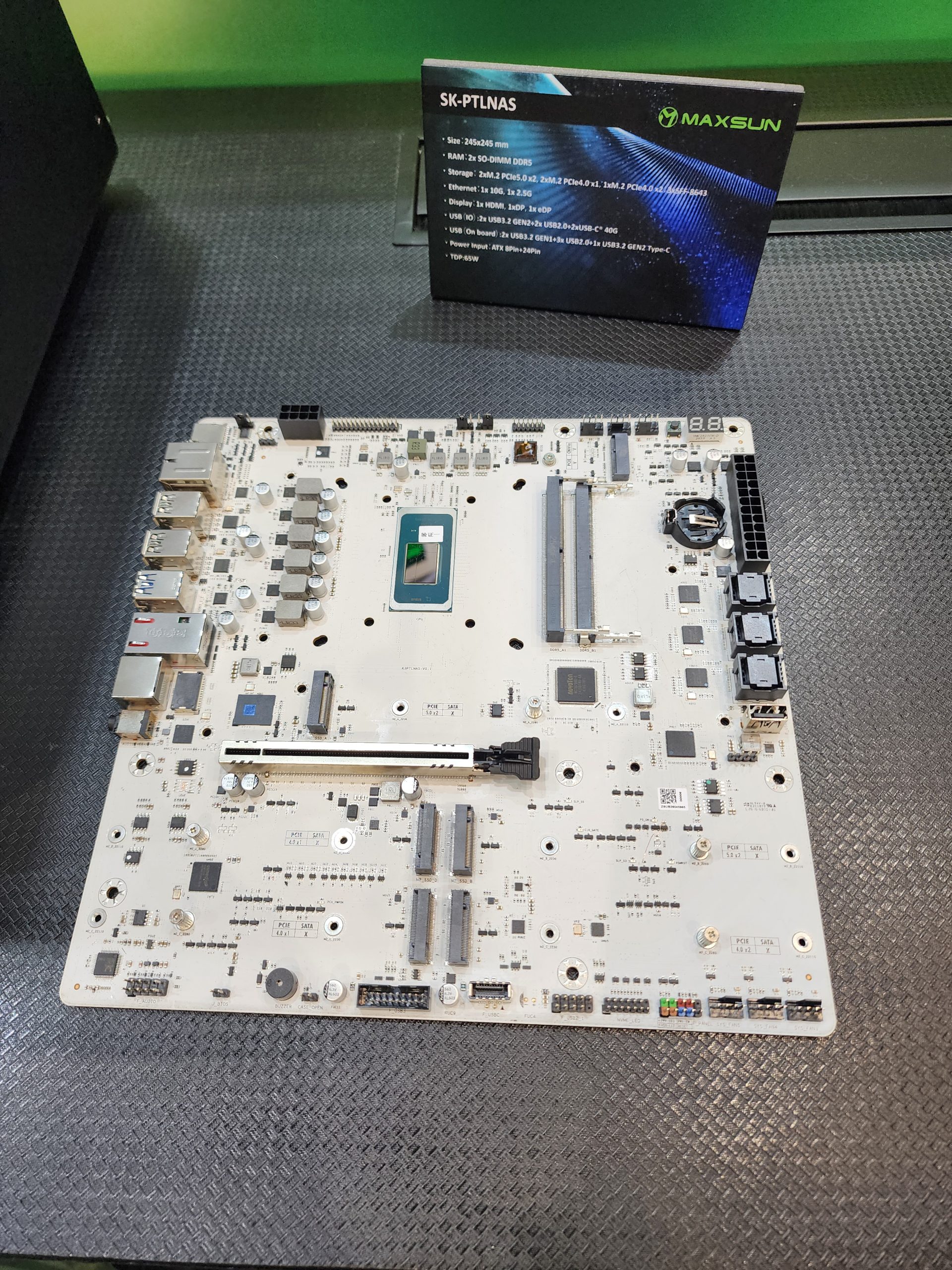 A Maxsun motherboard labeled SK-PTLNAS is displayed on a table, with a detailed specification card listing features such as '2x M.2 PCIe3.0 x4,' 'HDMI,' and 'TDP: 55W.'