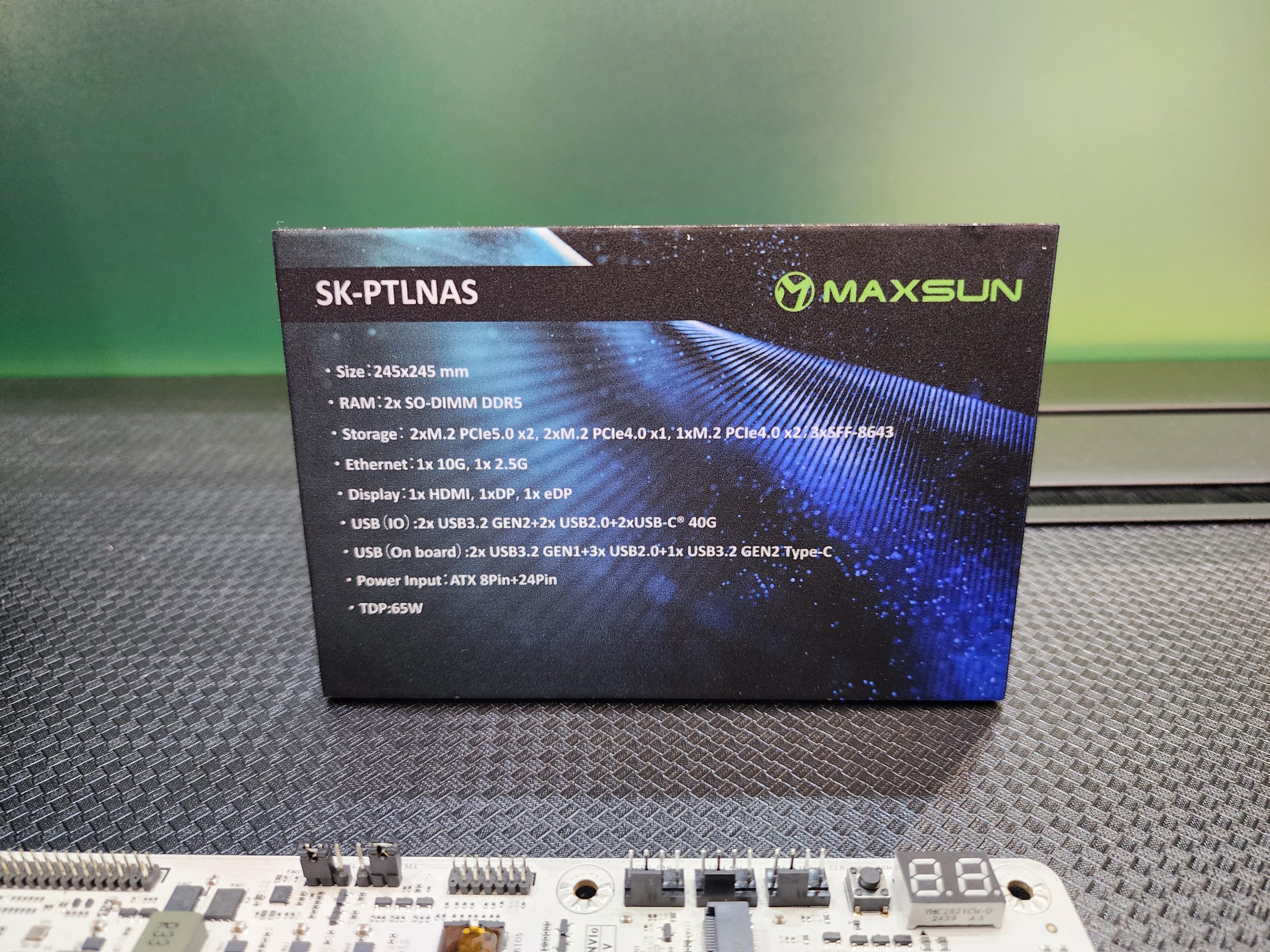 A Maxsun SK-PTLNAS motherboard box lists specifications including 'RAM: 2x SO-DIMM DDR5', various USB, Ethernet, and display options, alongside a partially visible motherboard.