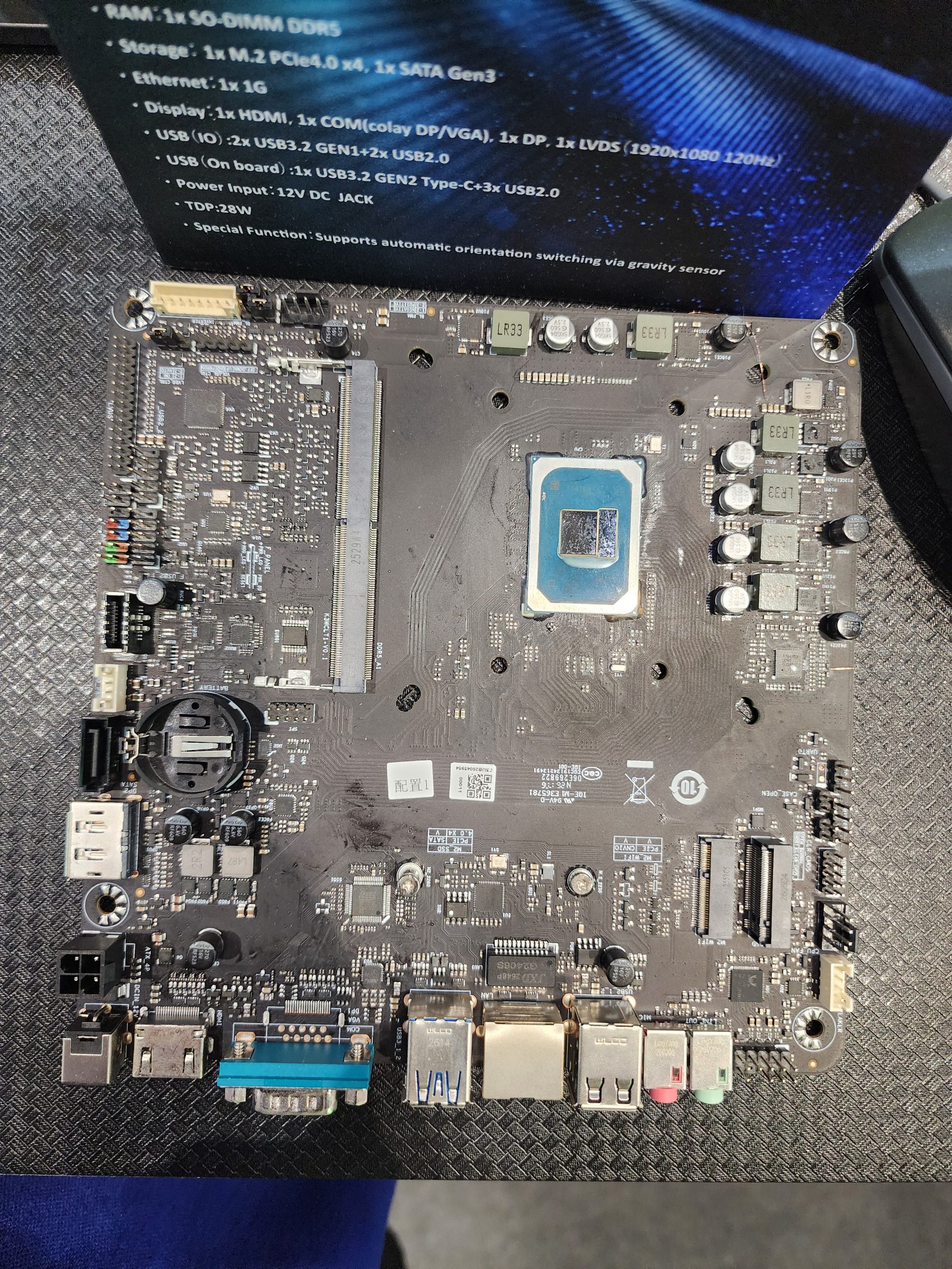 A bare motherboard with an exposed Intel CPU socket is displayed alongside on-screen specification text detailing features such as '1x SO-DIMM DDR5,' '1x M.2 PCIe4.0 x4,' and video output options.