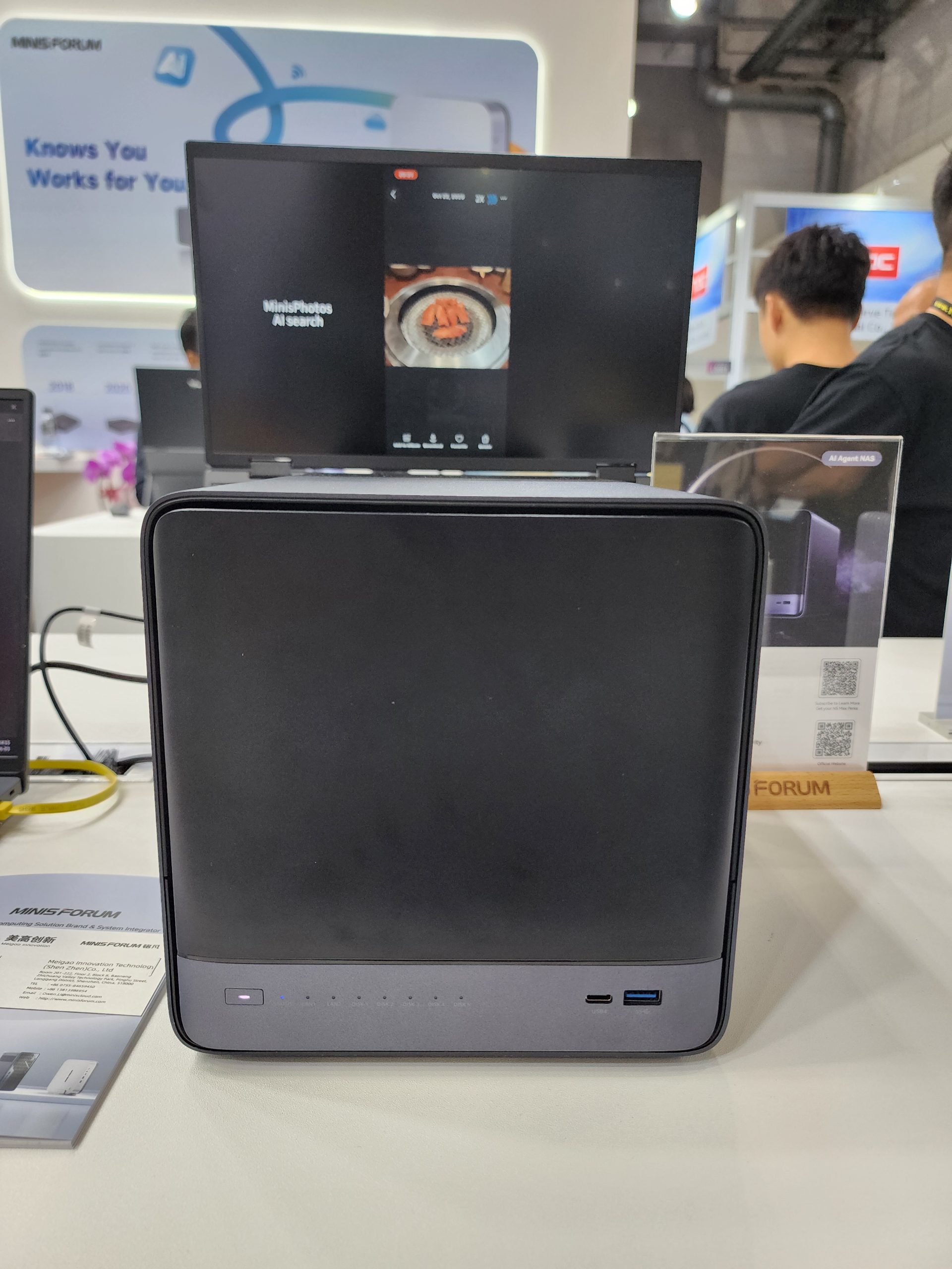 A MINISFORUM device on display with a screen showing 'MinisPhotos AI search' featuring an image of food.