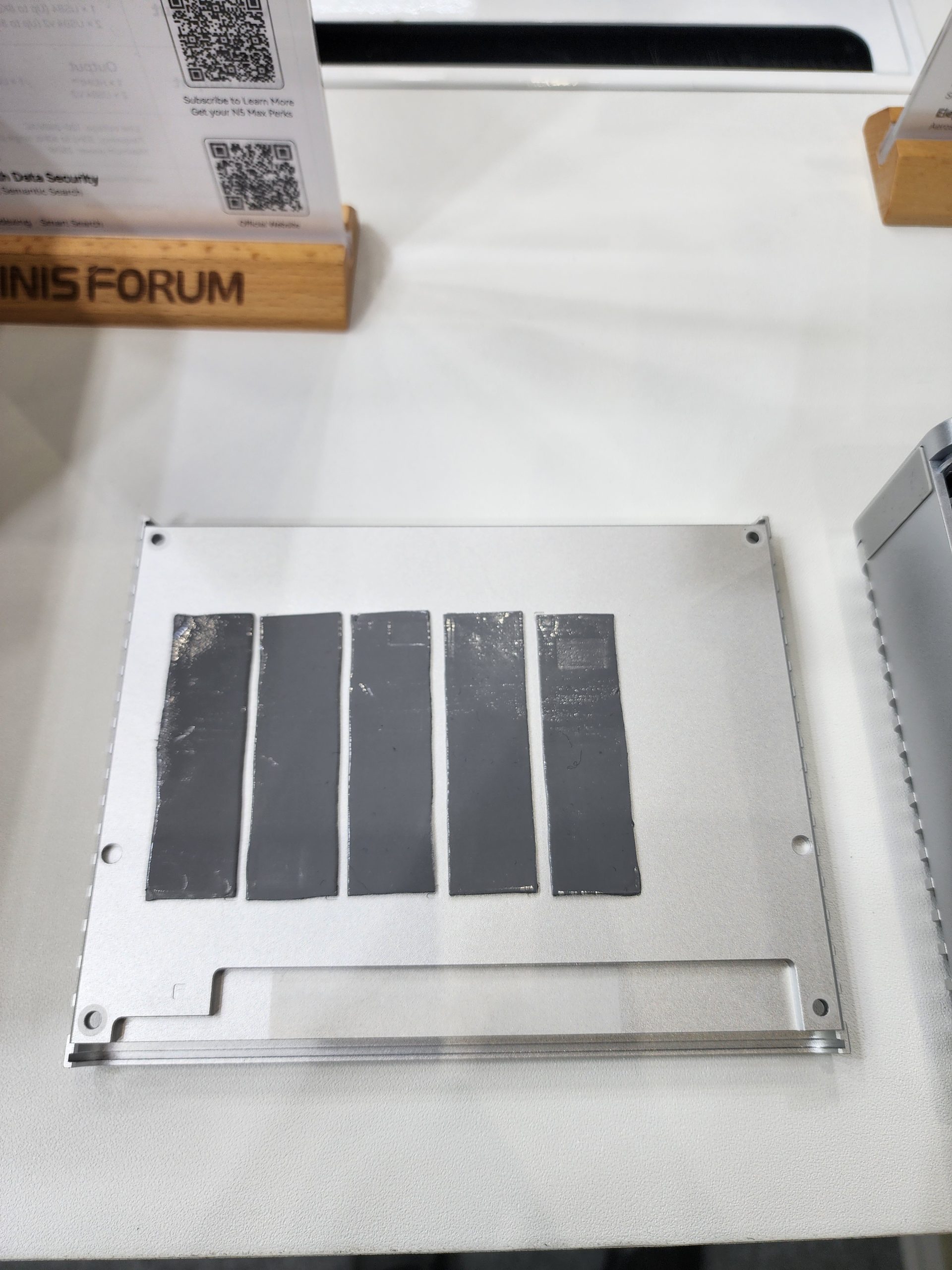 A metal heat spreader with dark thermal pads is displayed on a table next to a Minisforum branded sign.