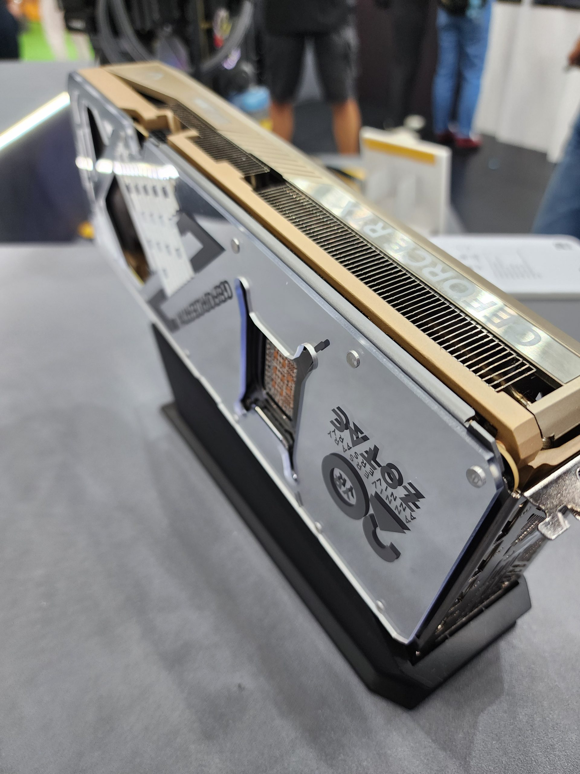A close-up view of a Zotac GeForce RTX graphics card with a silver and gold heatsink design on display at an event.