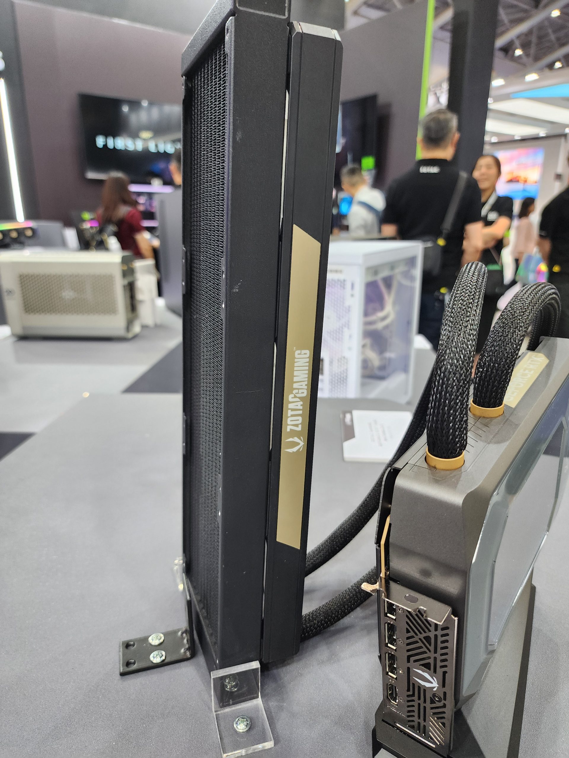 A Zotac Gaming GPU with cooling system is displayed vertically at a tech exhibition.