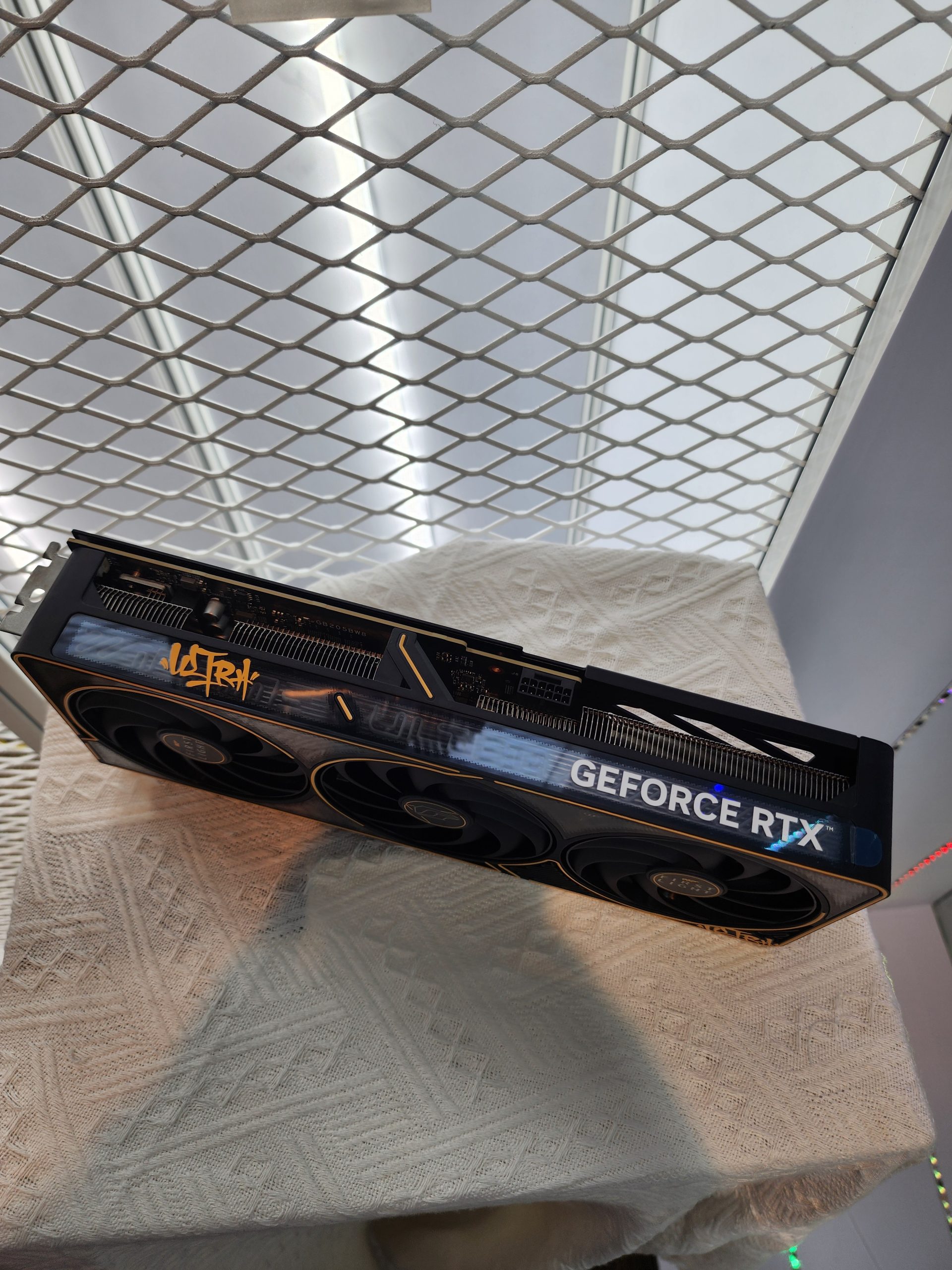An NVIDIA GeForce RTX graphics card featuring triple fans and 'ASRock' branding is displayed on a textured surface.