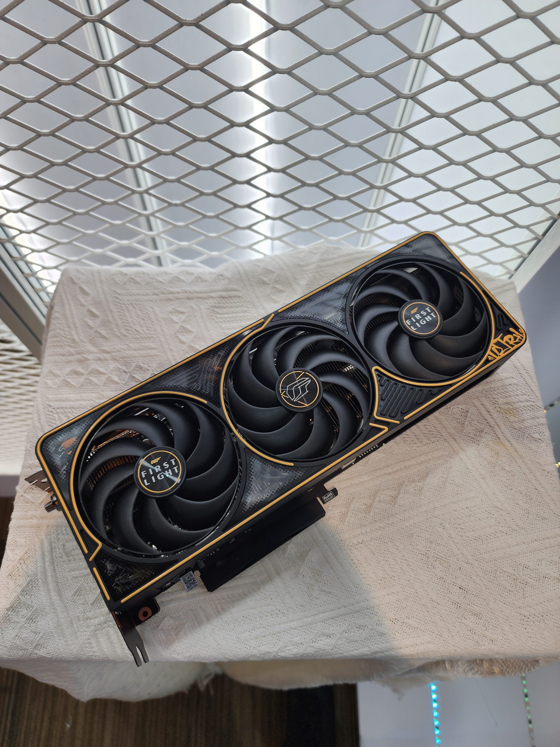 An ASRock graphics card labeled 'FIRST FLIGHT' with three cooling fans displayed on a white textured fabric.