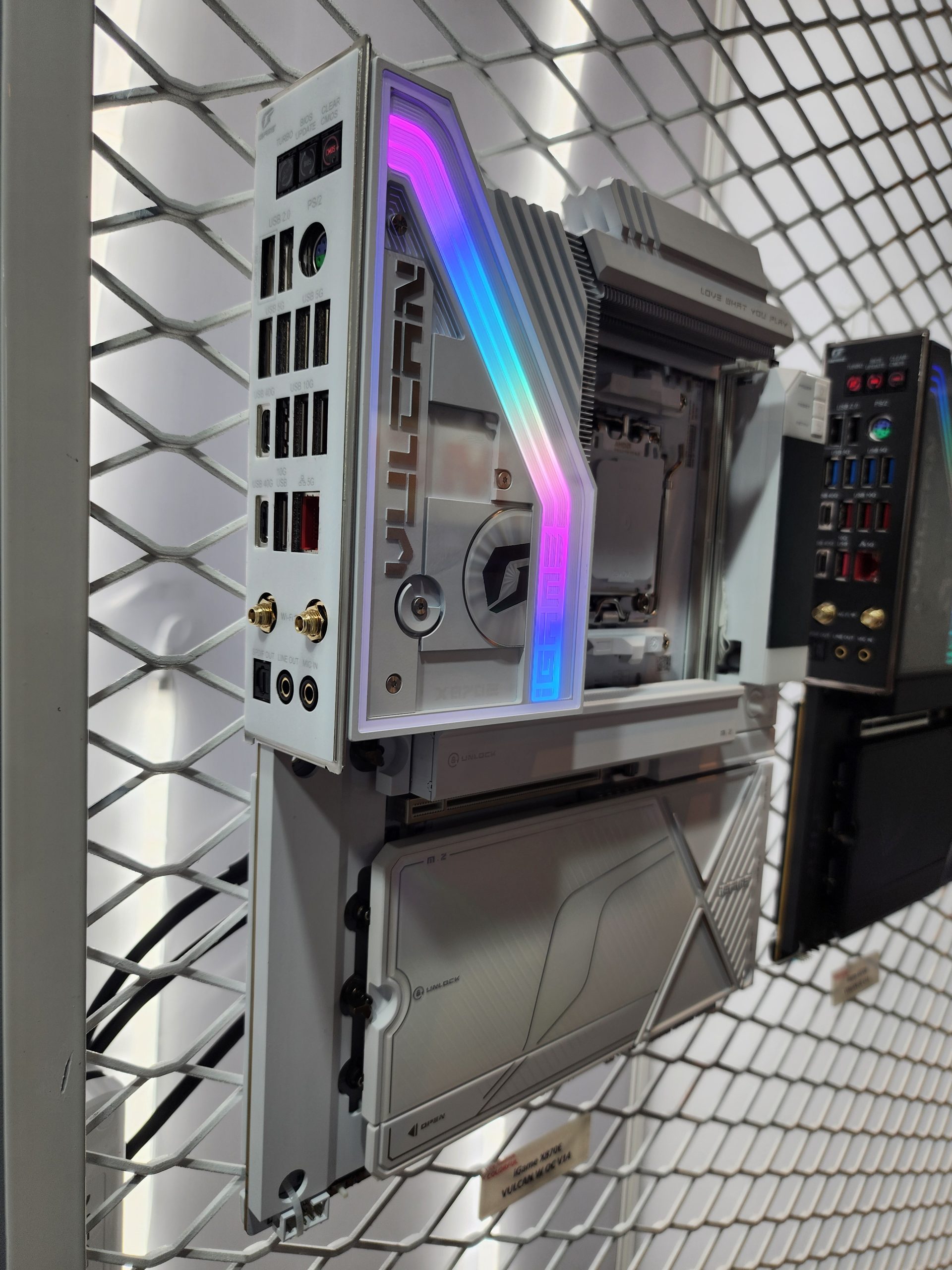A white ASUS TUF Gaming Z790 GT10 motherboard with RGB lighting displayed on a mesh wall, featuring multiple USB ports and audio jacks.