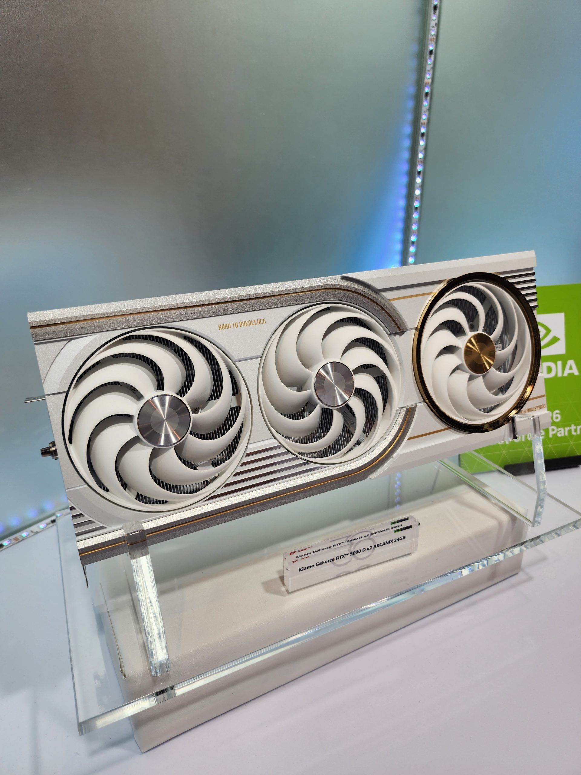 A Colorful iGame GeForce RTX 5090 Vulcan graphics card with three fans is displayed on a stand with a label reading 'iGame GeForce RTX 5090 V2 ADACNZ 24GB'.