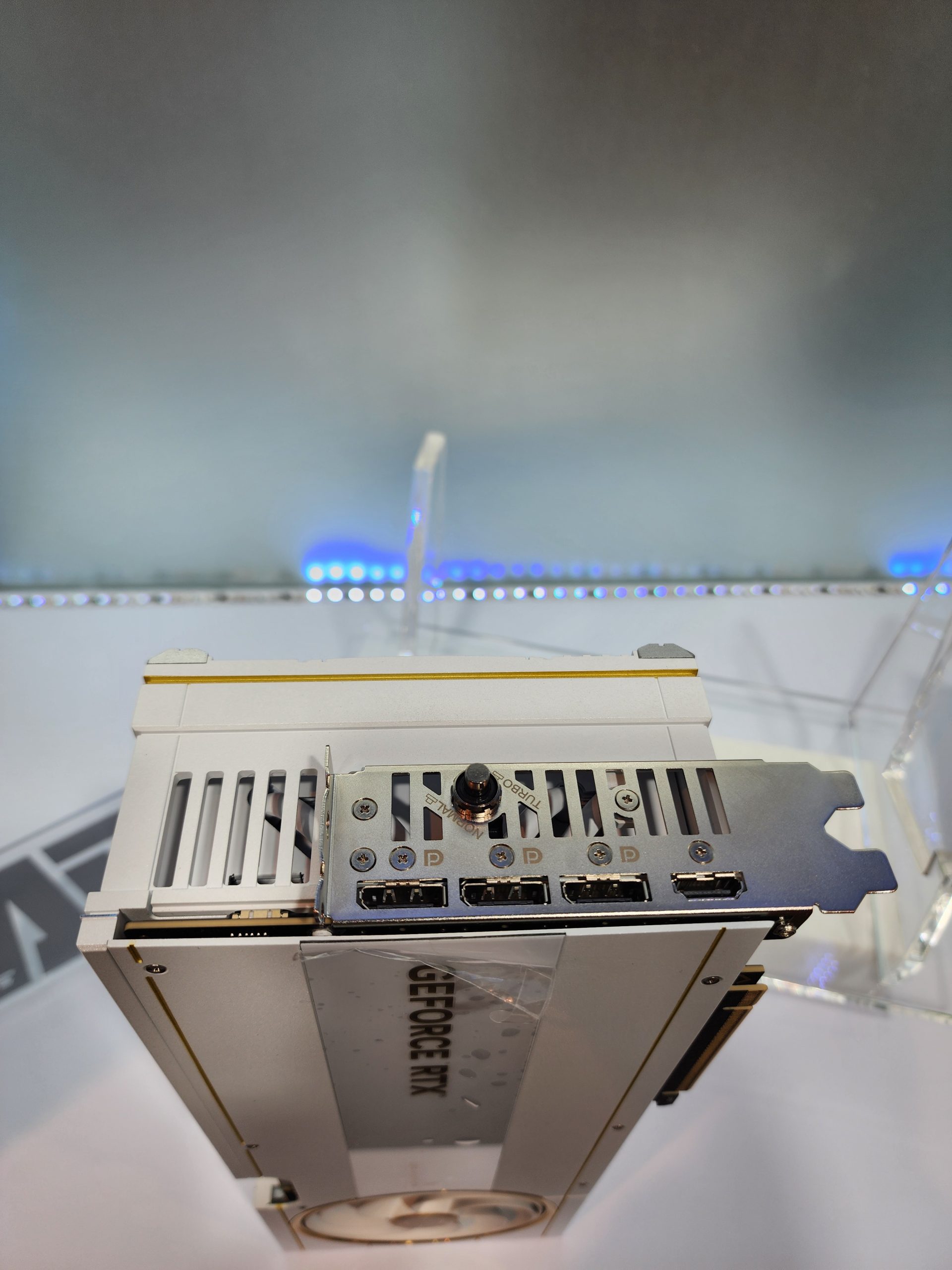 A white NVIDIA GeForce RTX graphics card with multiple DisplayPorts and an HDMI port is on display, featuring 'GEFORCE RTX' text on the side.