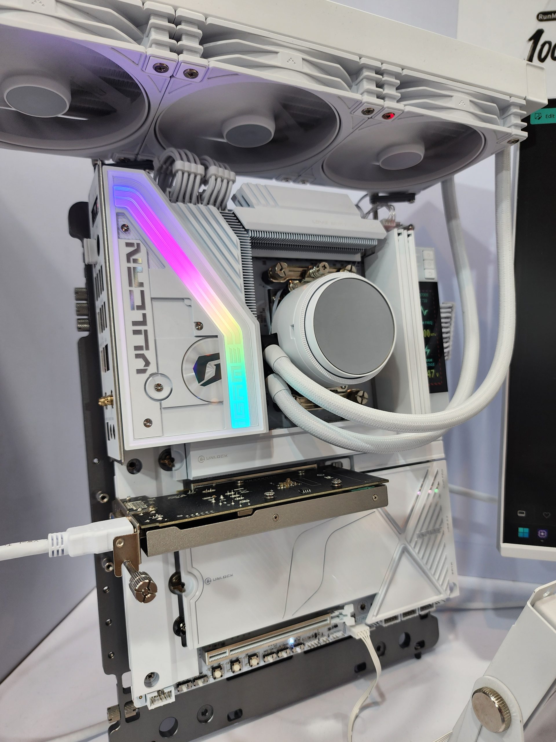 A white custom PC build with Lian Li components, featuring a 'VULCAN' RGB-lit element, and a visible water cooling system, mounted on a test bench.