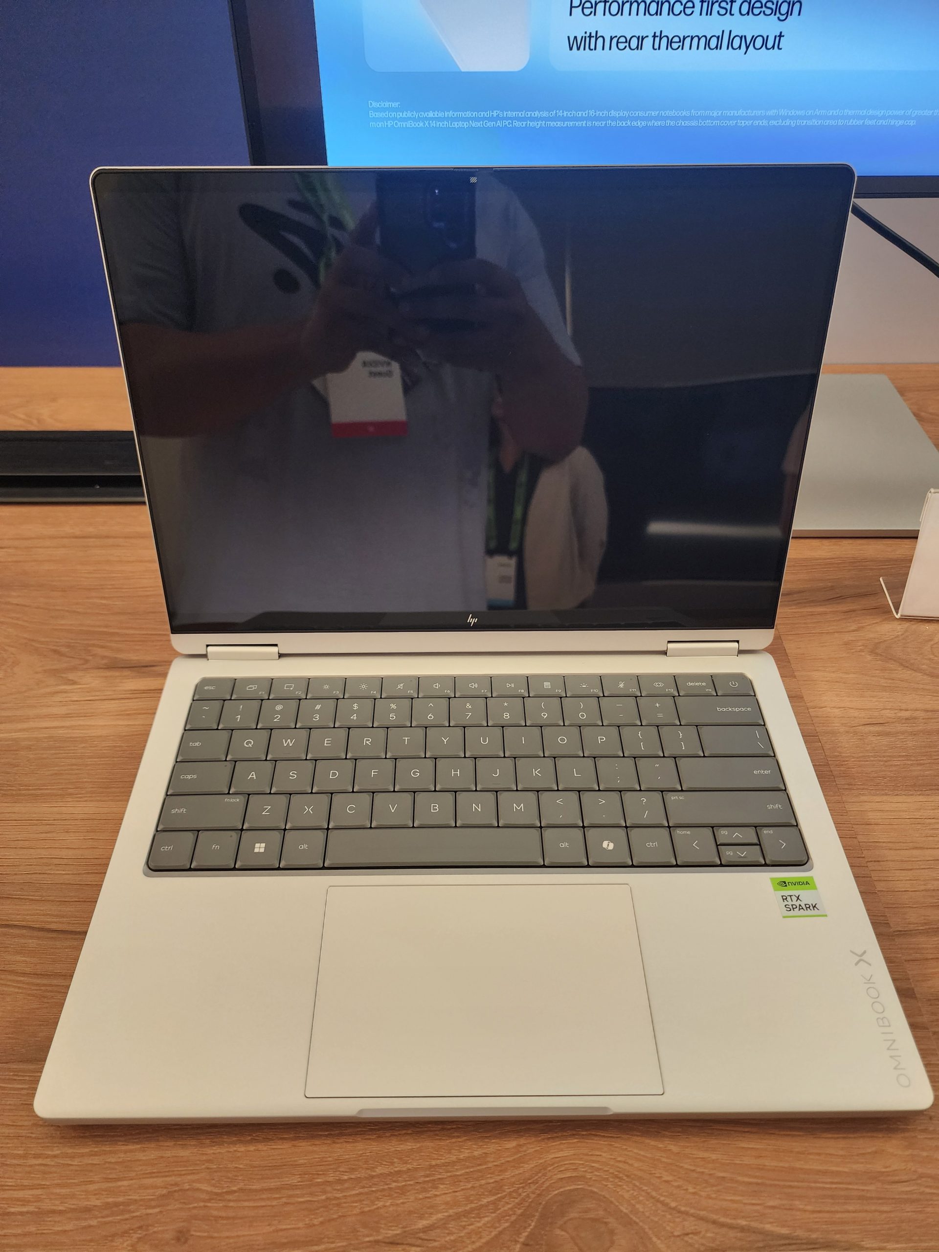 An HP Omnibook X laptop is displayed on a wooden table, featuring an NVIDIA RTX Spark sticker next to the keyboard.