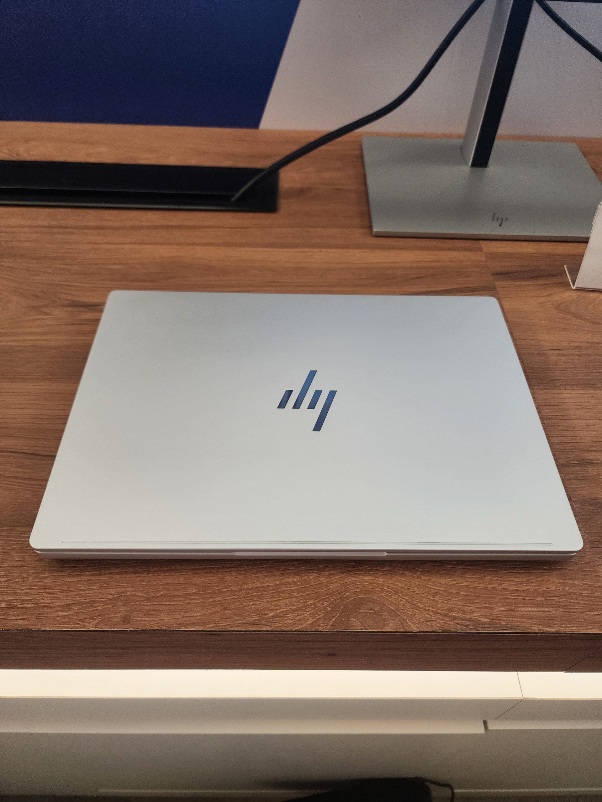 A silver HP laptop with a stylized hp logo on the cover, placed on a wooden desk next to an HP monitor.