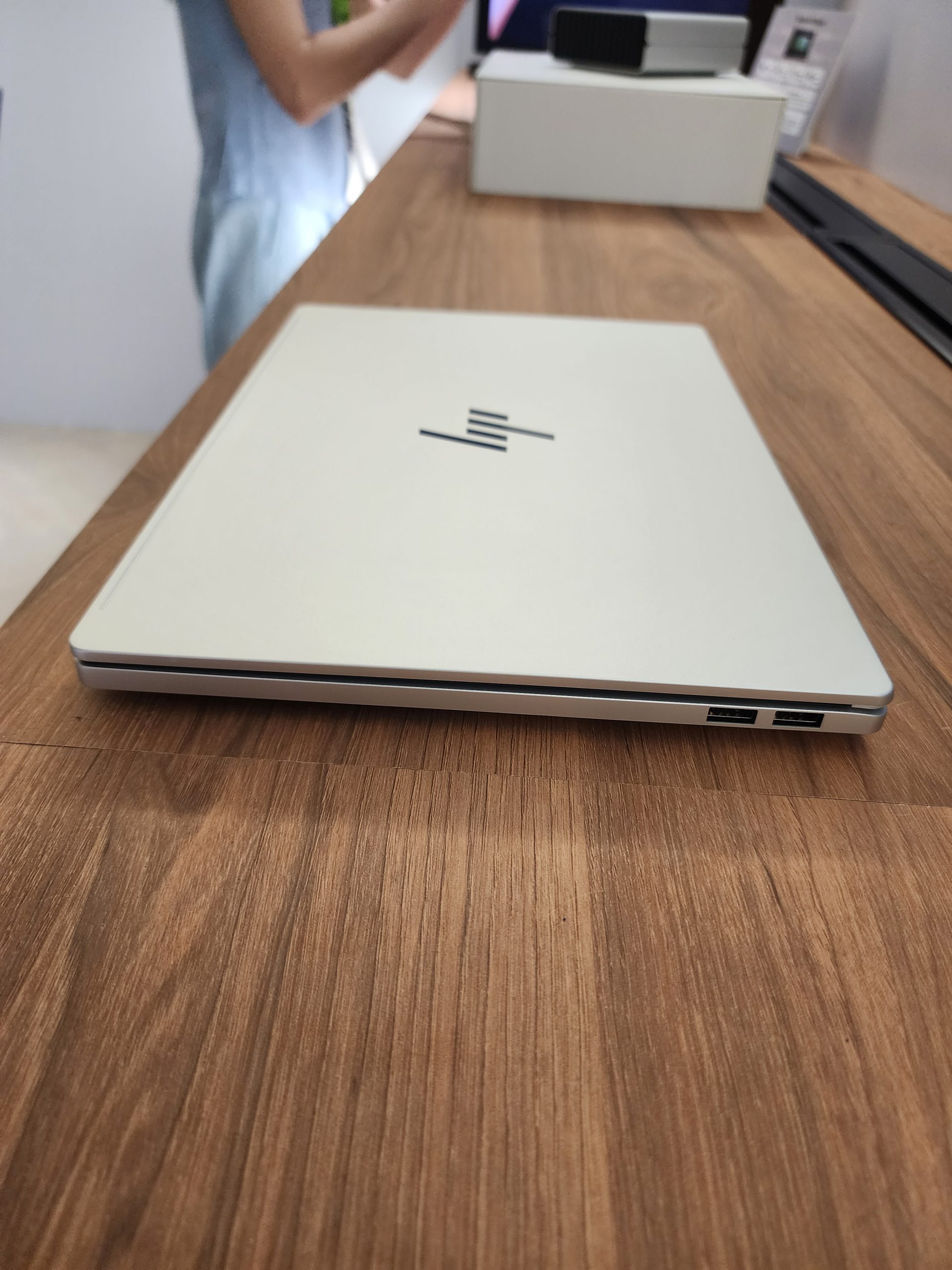 A white HP laptop with its logo visible lies closed on a wooden table, alongside other tech items in the background.